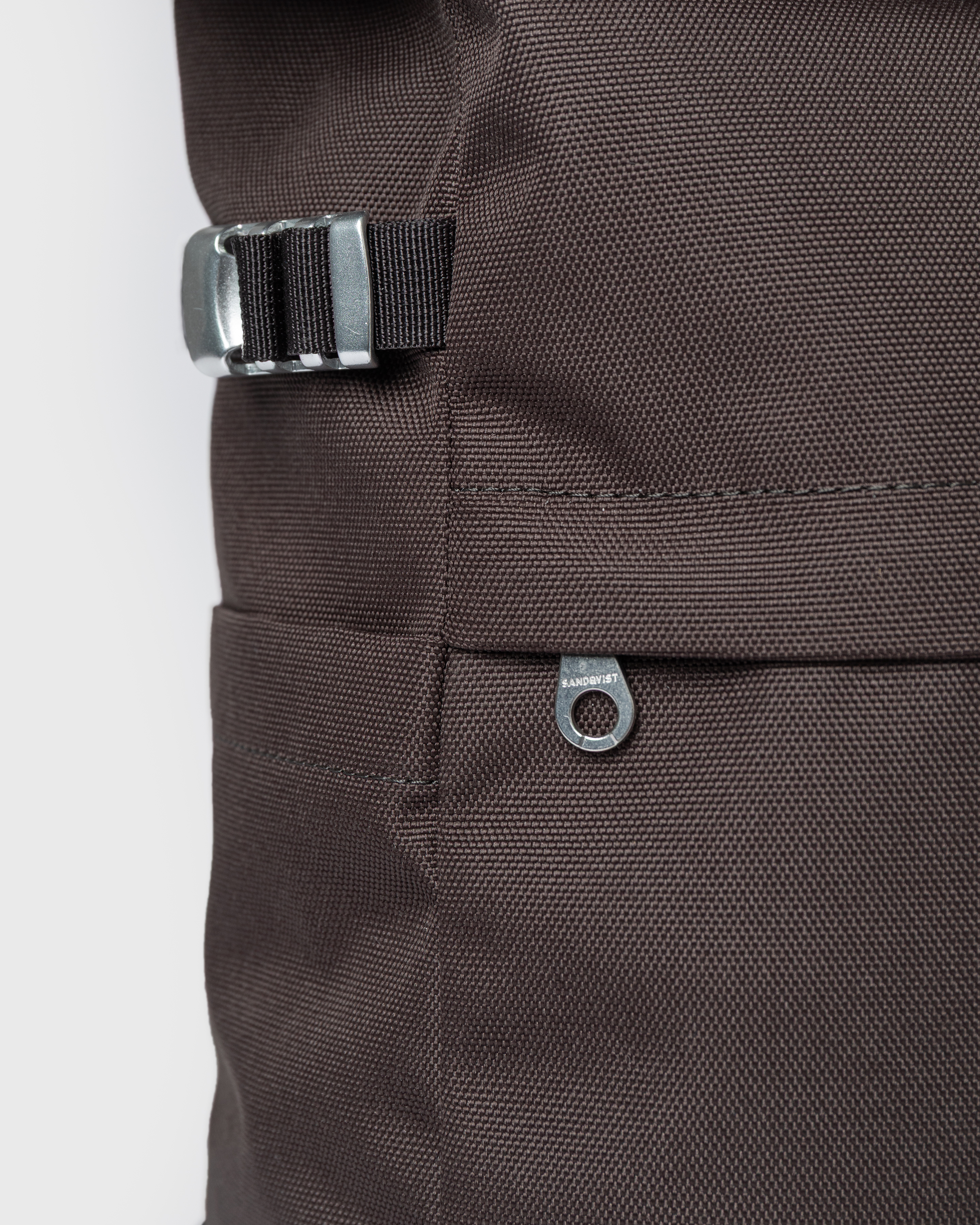 Close up view of adjustable strap, side slip pocket and outer zipper pocket on the backpack Sandqvist ICON Rolltop Backpack M 14" in brown.