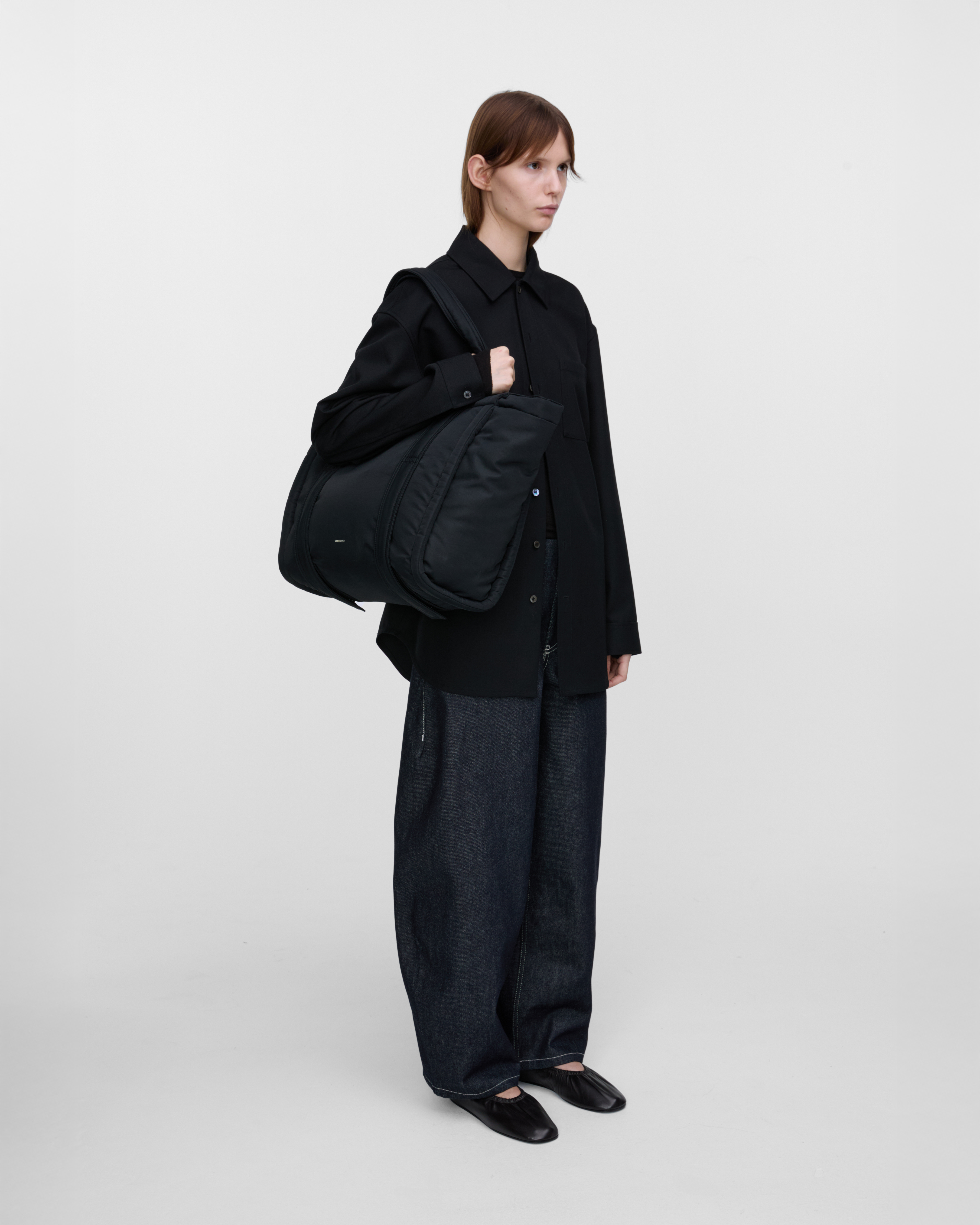 Female model wearing Sandqvist Curve Tote Bag, black. Front view, wearing the bag on one shoulder.