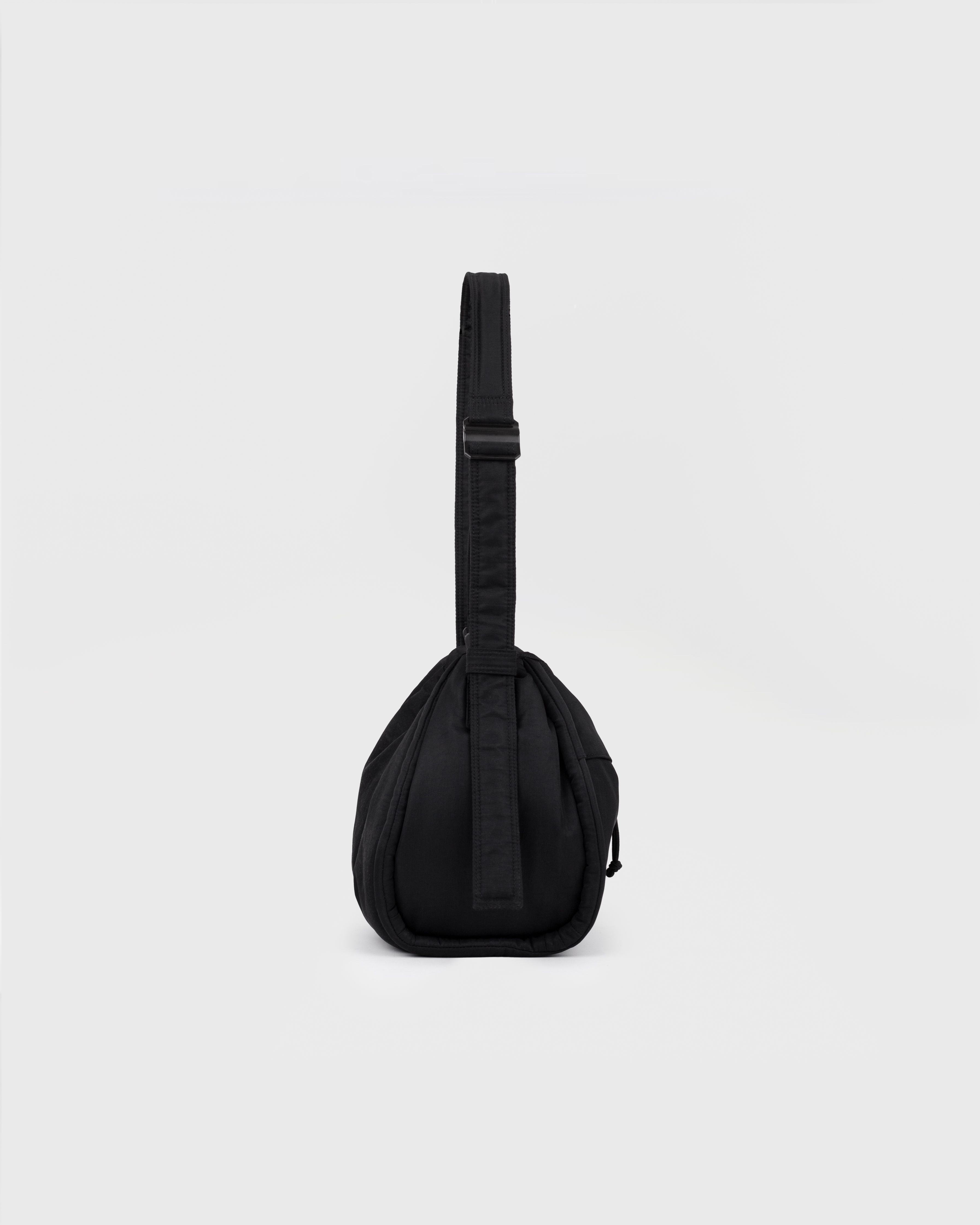 Side view of Sandqvist Curve Bucket Bag, black, in a standing position with the strap showing.