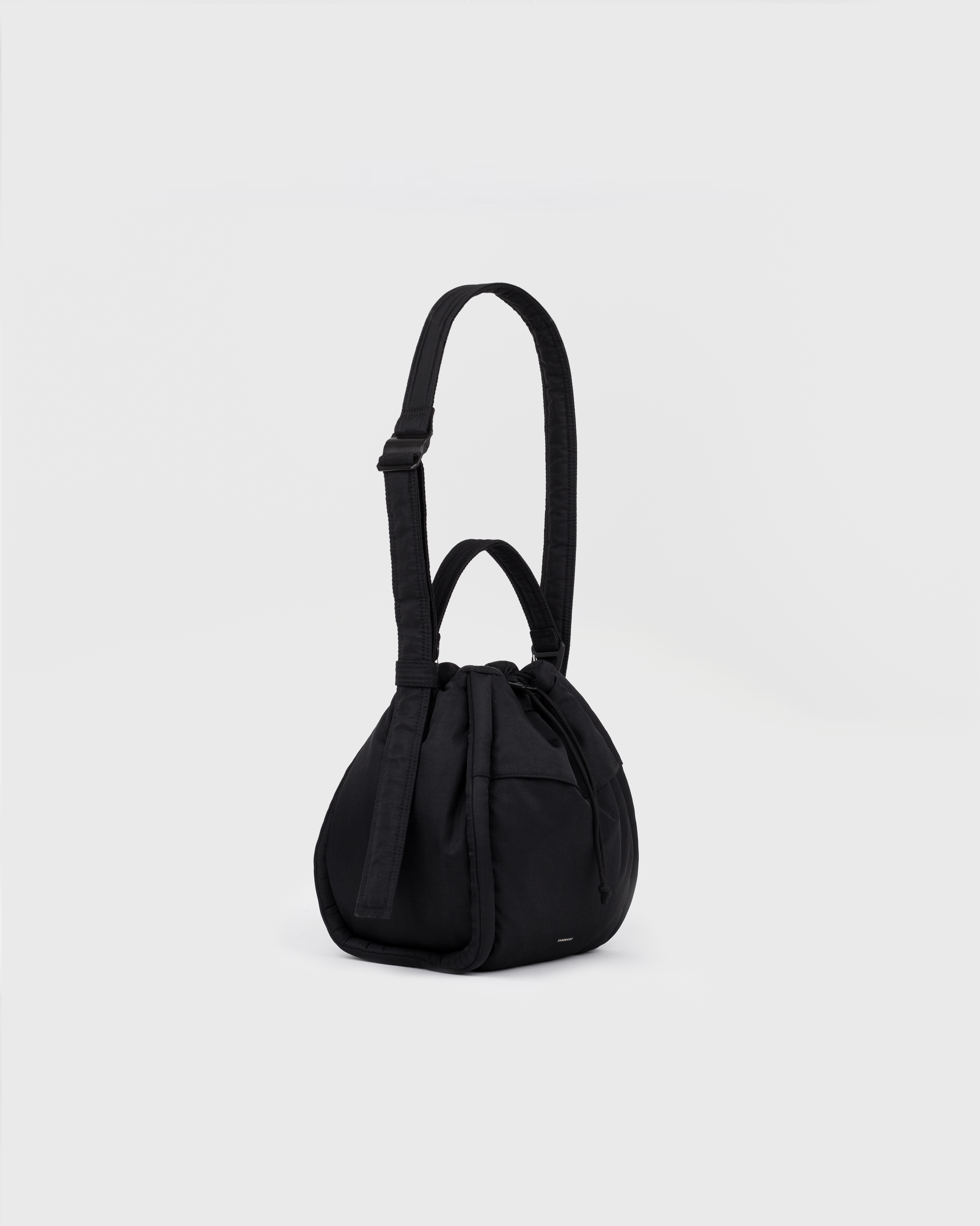 View of Sandqvist Curve Bucket Bag, black, in a standing position with the handle and strap showing.