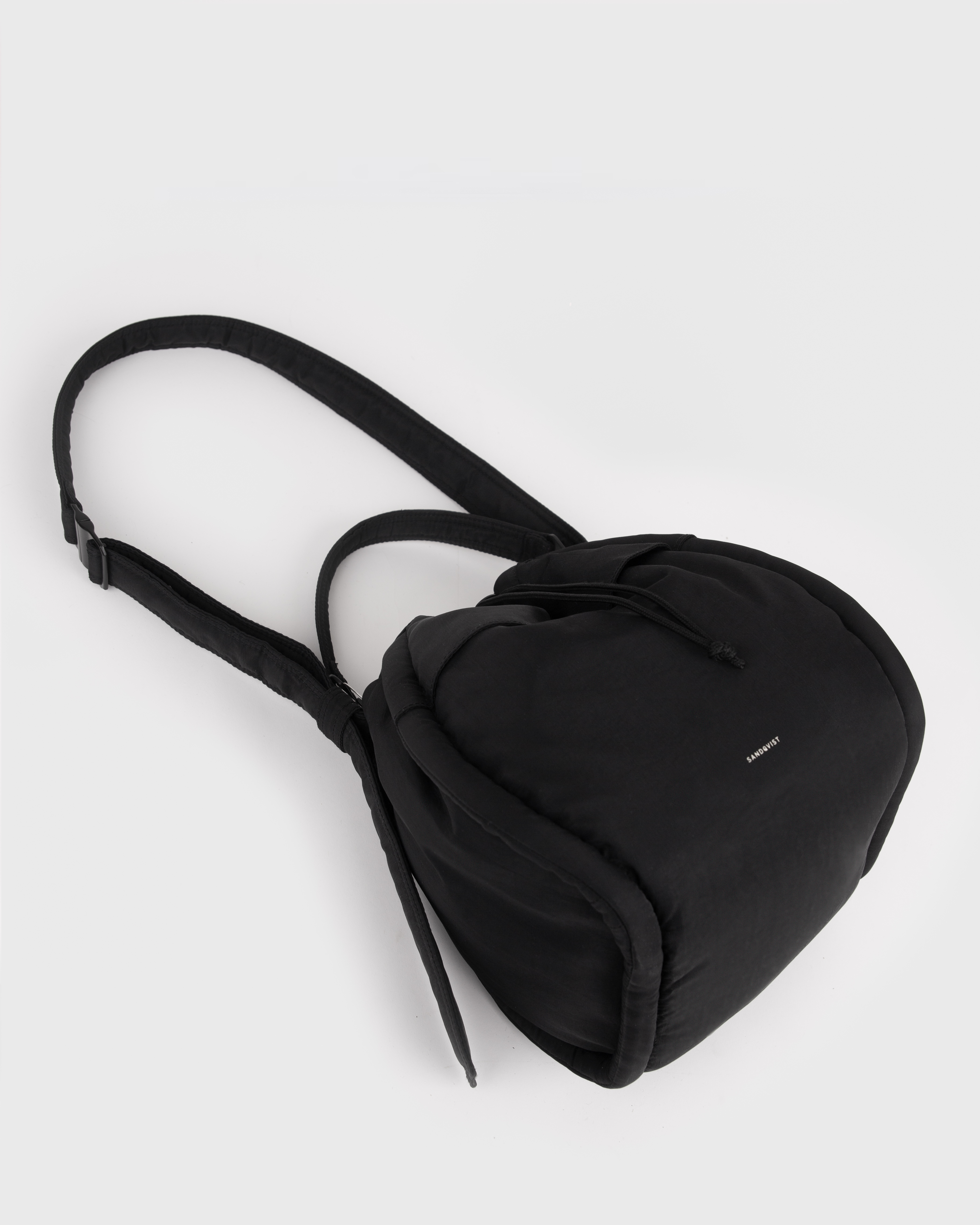 View of Sandqvist Curve Bucket Bag, black, lying down with the handle and strap showing.