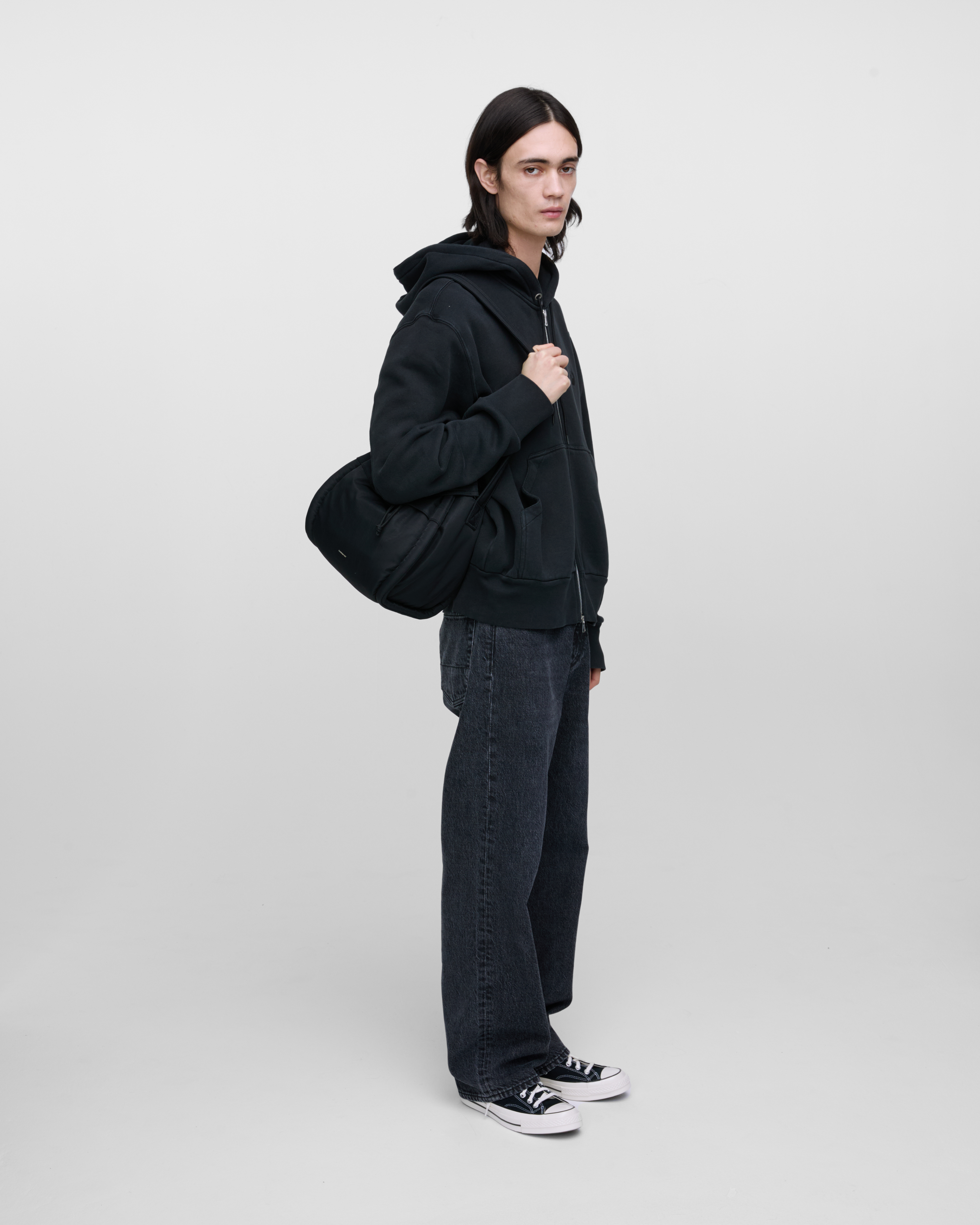 Male model wearing Sandqvist Curve Bucket Bag, black. Side view, carrying the bag on one shoulder crossbody.