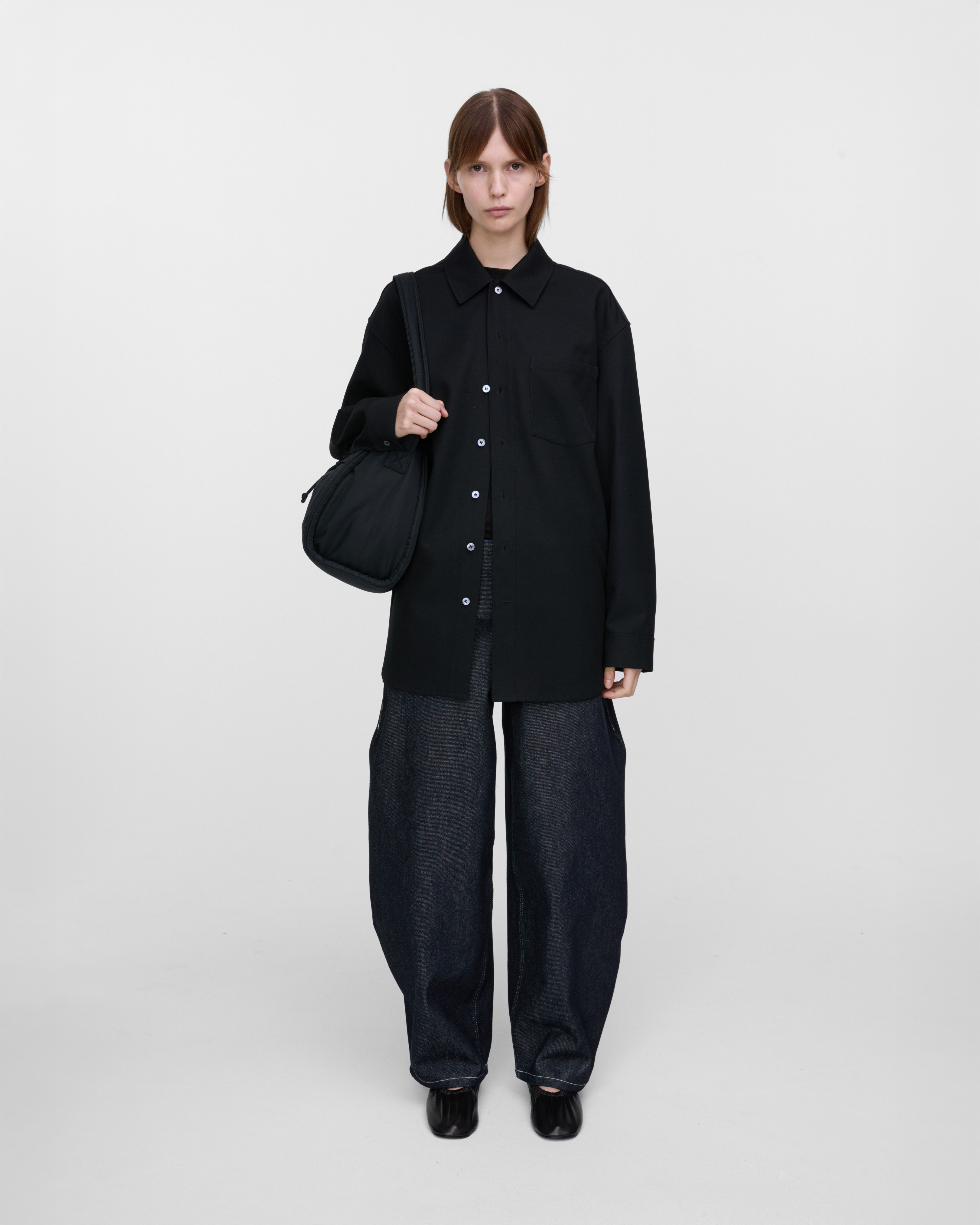 Female model wearing Sandqvist Curve Bucket Bag, black. Front view, carrying the bag on one shoulder.