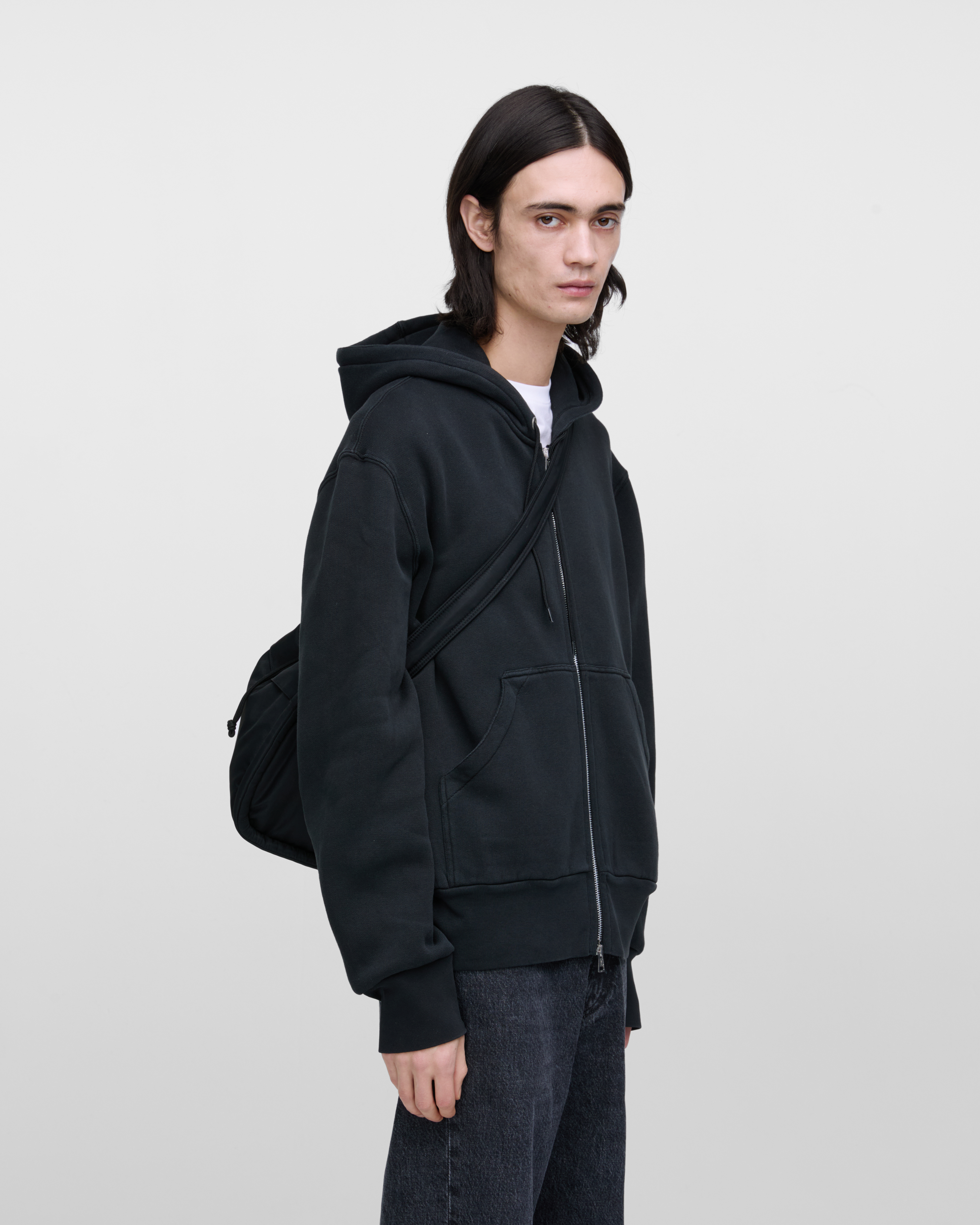 Male model wearing Sandqvist Curve Bucket Bag, black. Front view, carrying the bag on one shoulder crossbody.