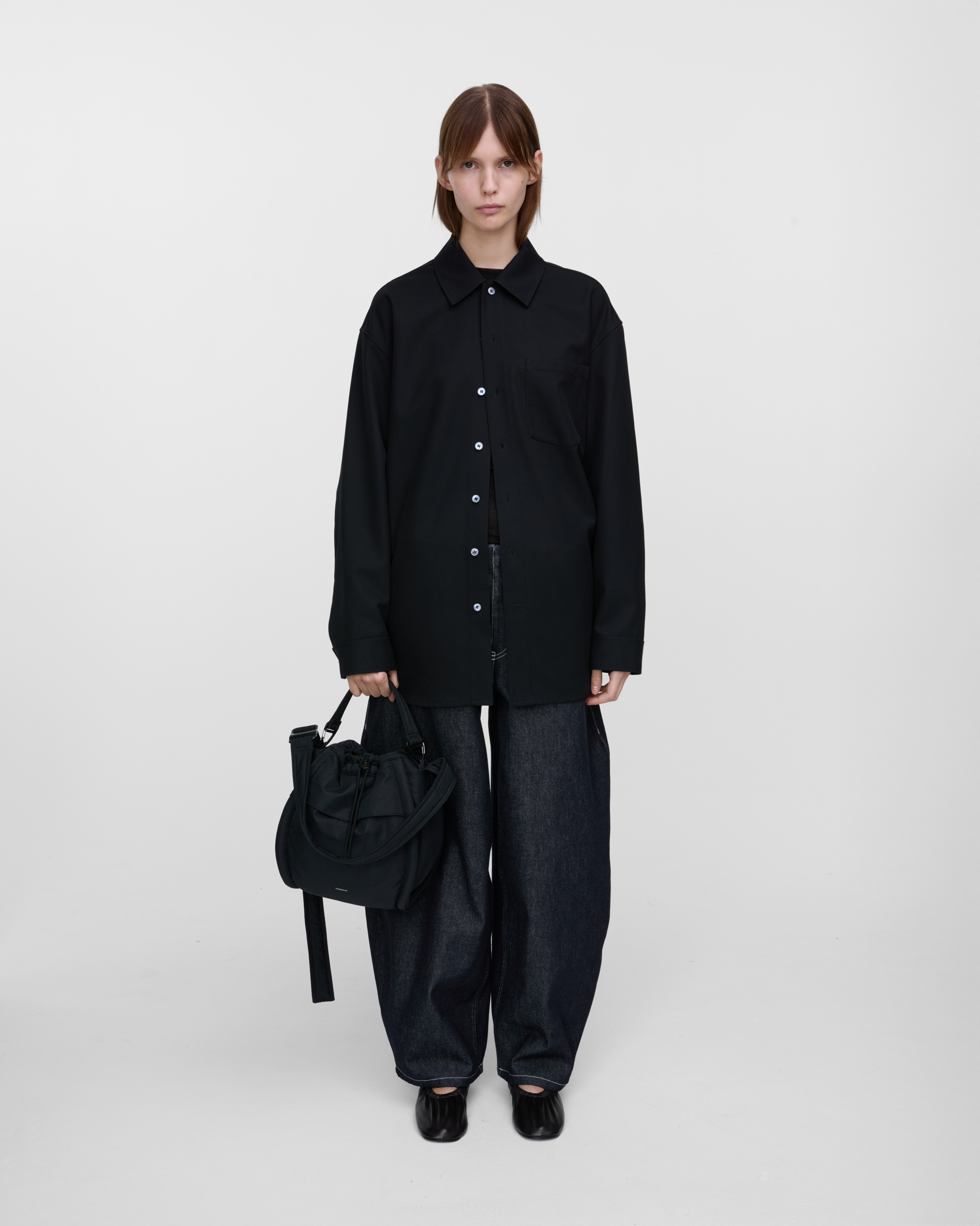 Female model holding Sandqvist Curve Bucket Bag, black. Front view, holding the bag in one hand.