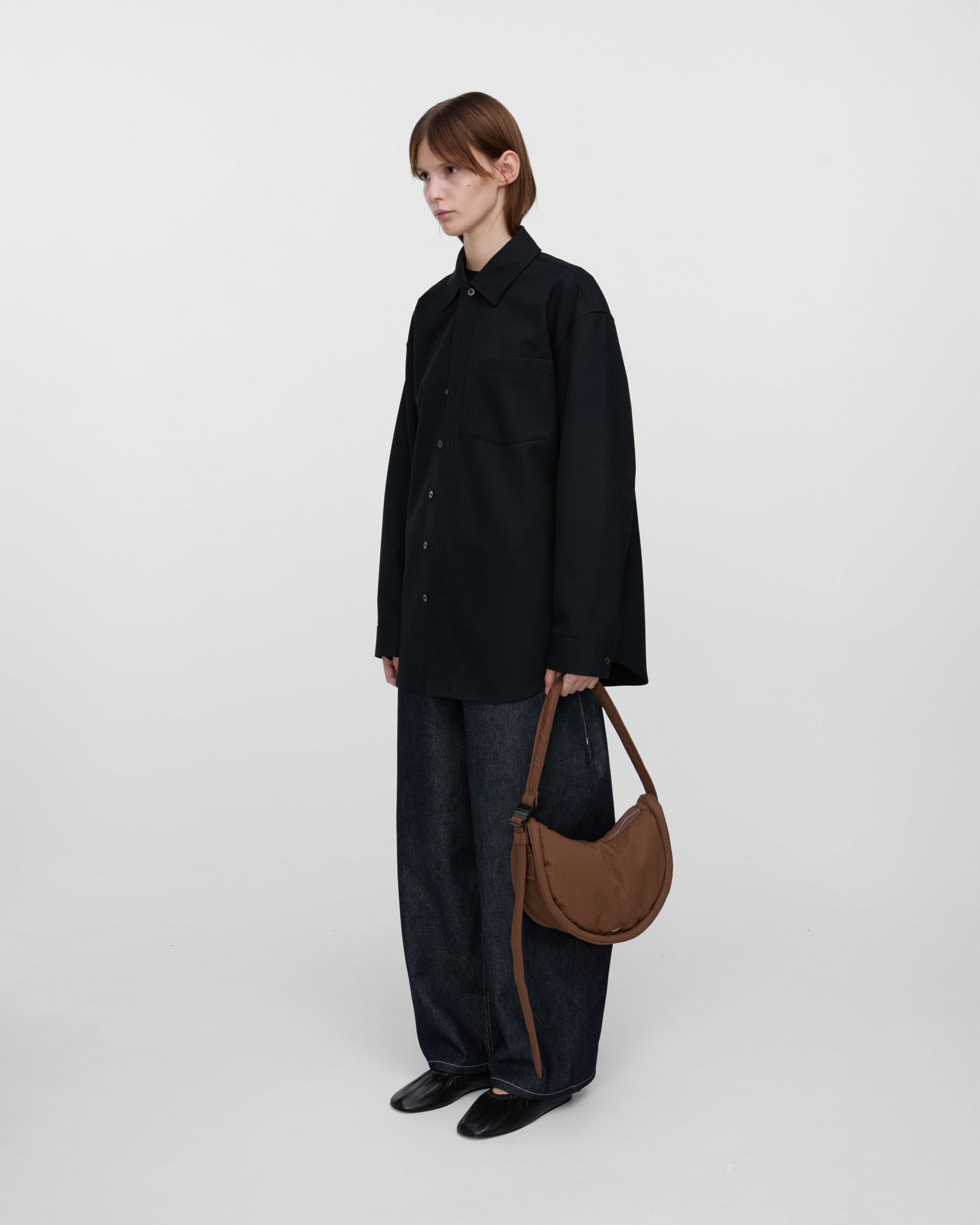 Female model holding Sandqvist Curve Half Moon Bag Mini, brown. Front view, holding the bag in one hand.
