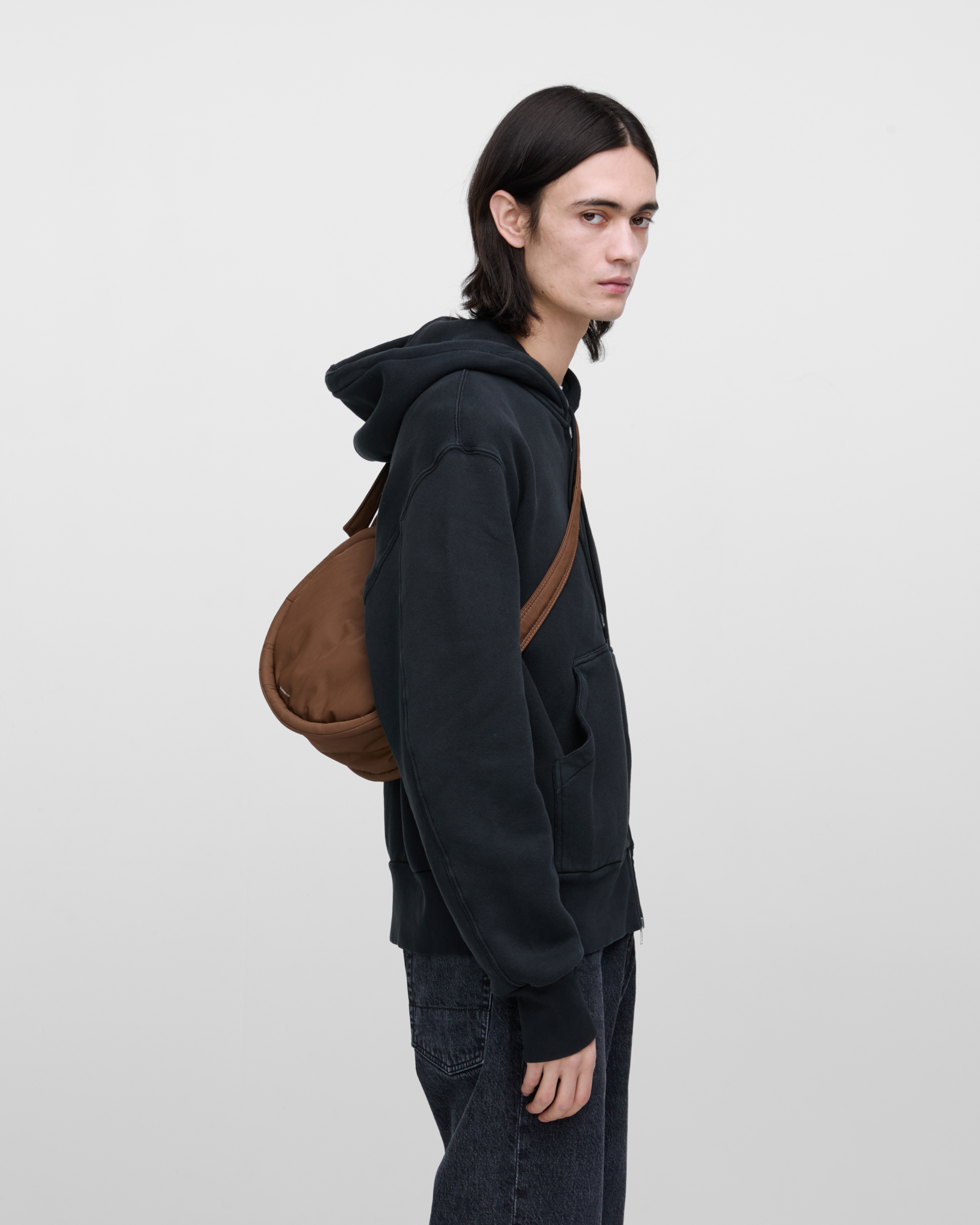 Male model carrying Sandqvist Curve Half Moon Bag Mini, brown. From behind, carrying the bag over one shoulder with the bag on his back.