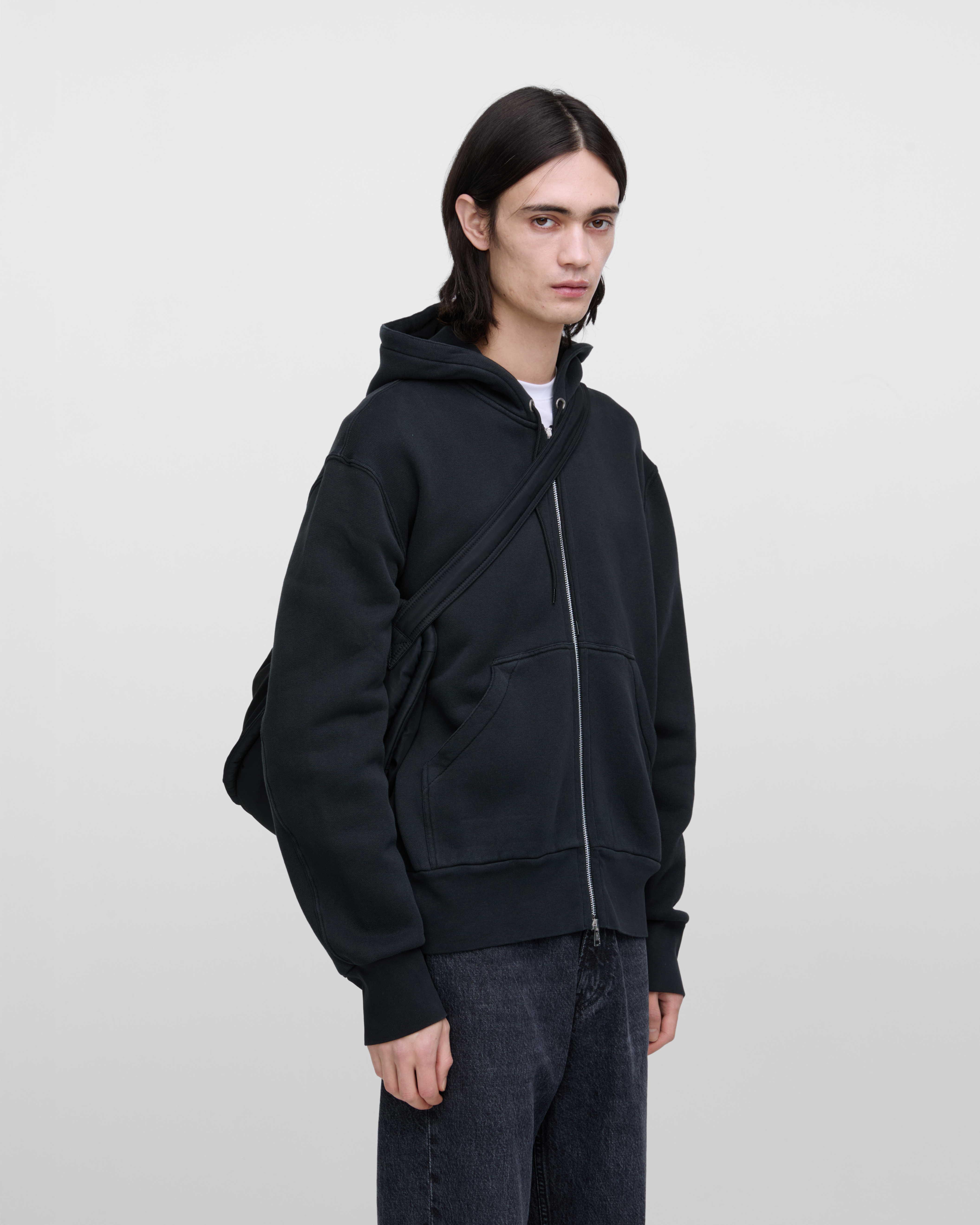 Male model carrying Sandqvist Curve Half Moon Bag, black. Front view, carrying the bag over one shoulder crossbody, with the bag in the back.