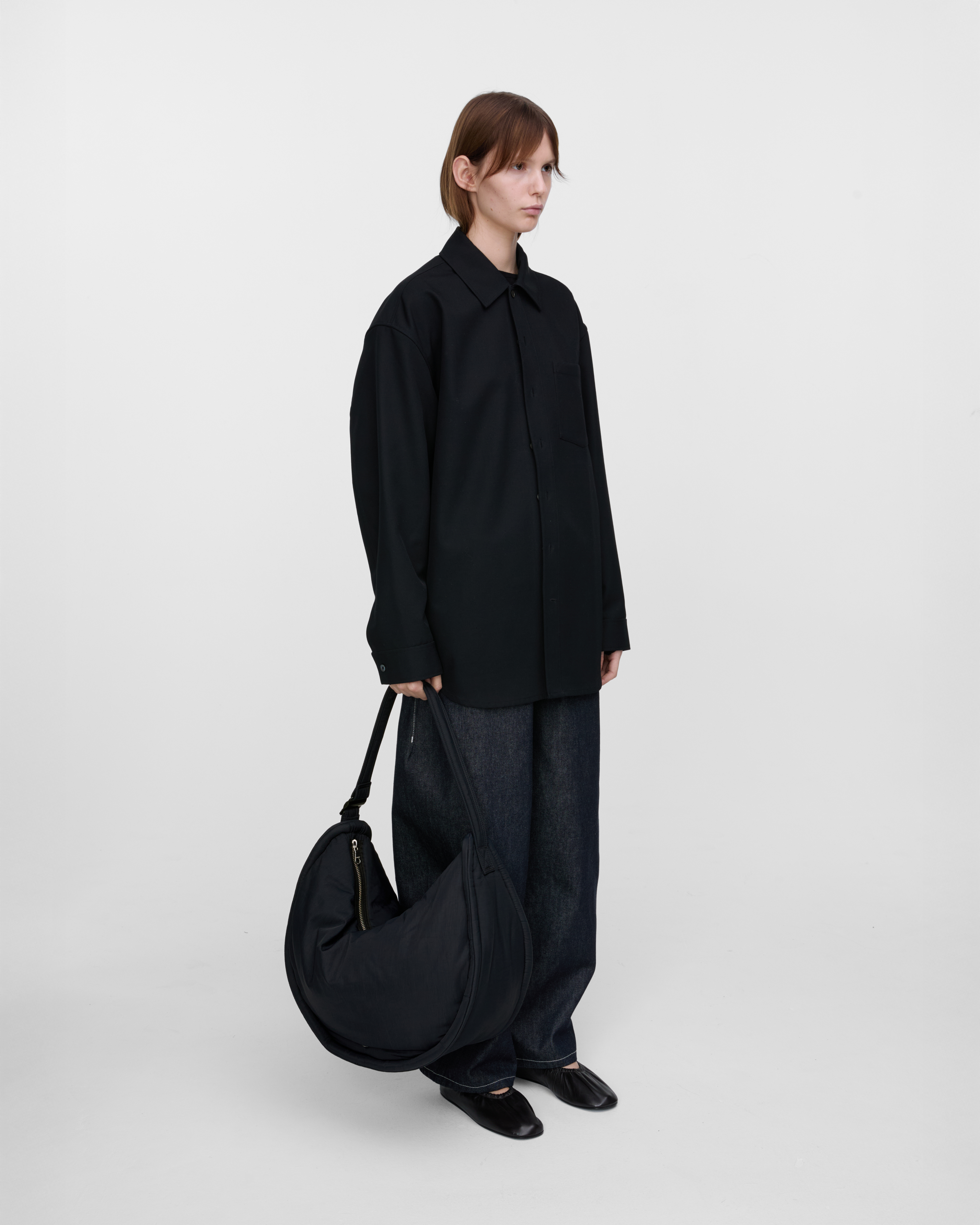 Female model holding Sandqvist Curve Half Moon Bag, black. Front view, holding the bag in one hand..