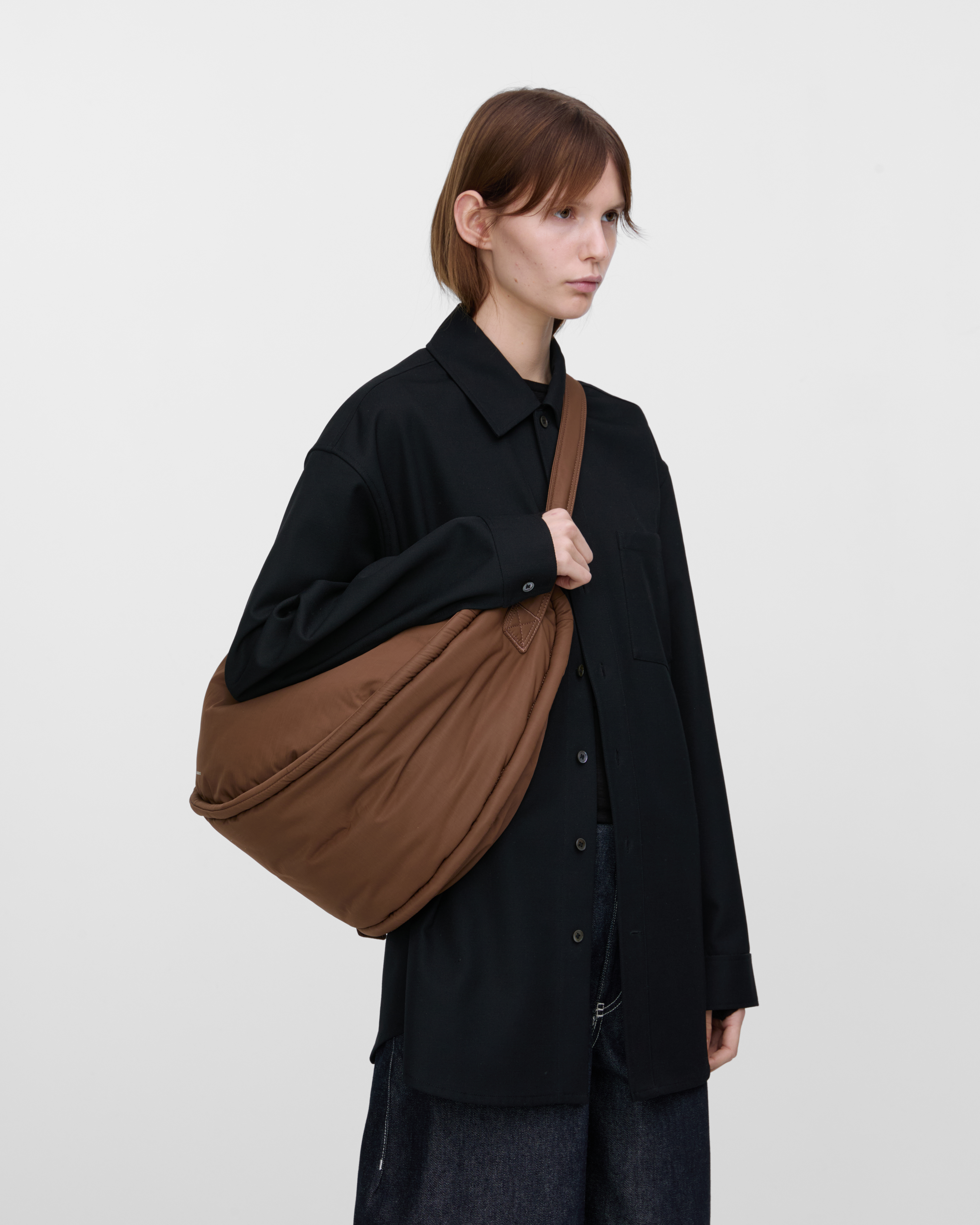 Weibliches Model mit Sandqvist Curve Half Moon Bag, braun. Seitenansicht, die Tasche über einer Schulter quer über den Körper getragen.