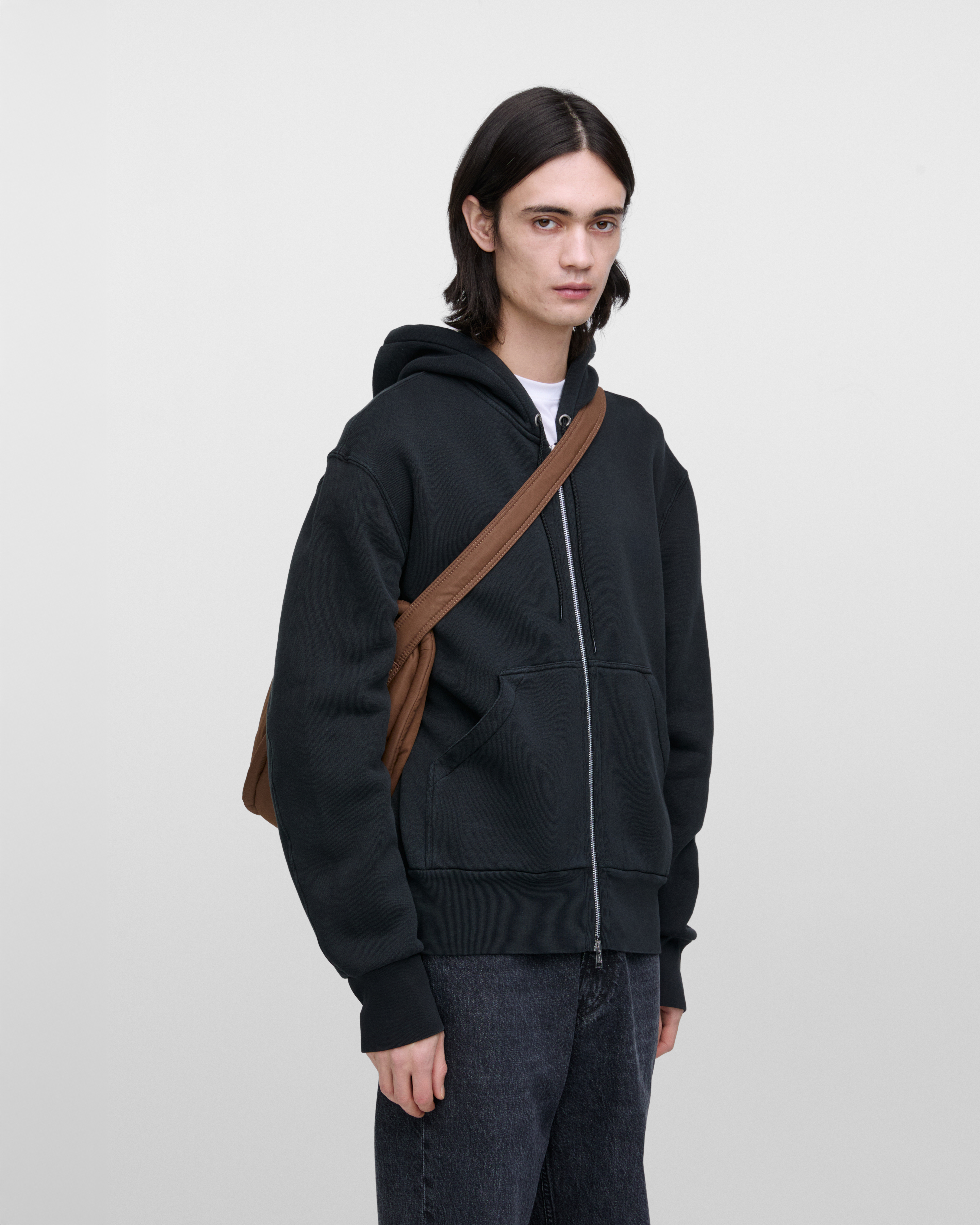 Männliches Model mit Sandqvist Curve Half Moon Bag, braun. Vorderansicht, die Tasche über einer Schulter quer über den Körper getragen.