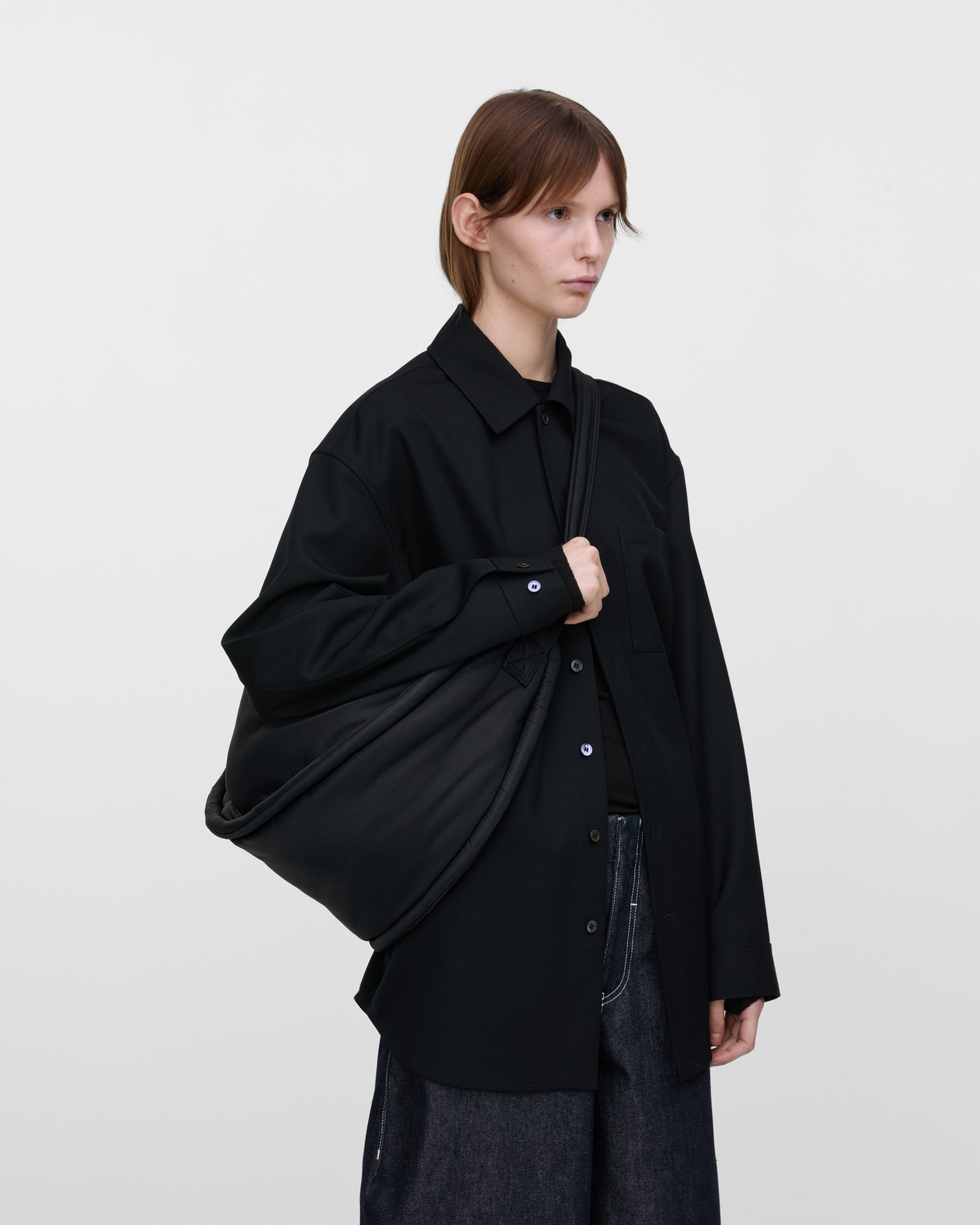 Female model wearing Sandqvist Curve Half Moon Bag, black. Side view, carrying the bag on one shoulder crossbody.