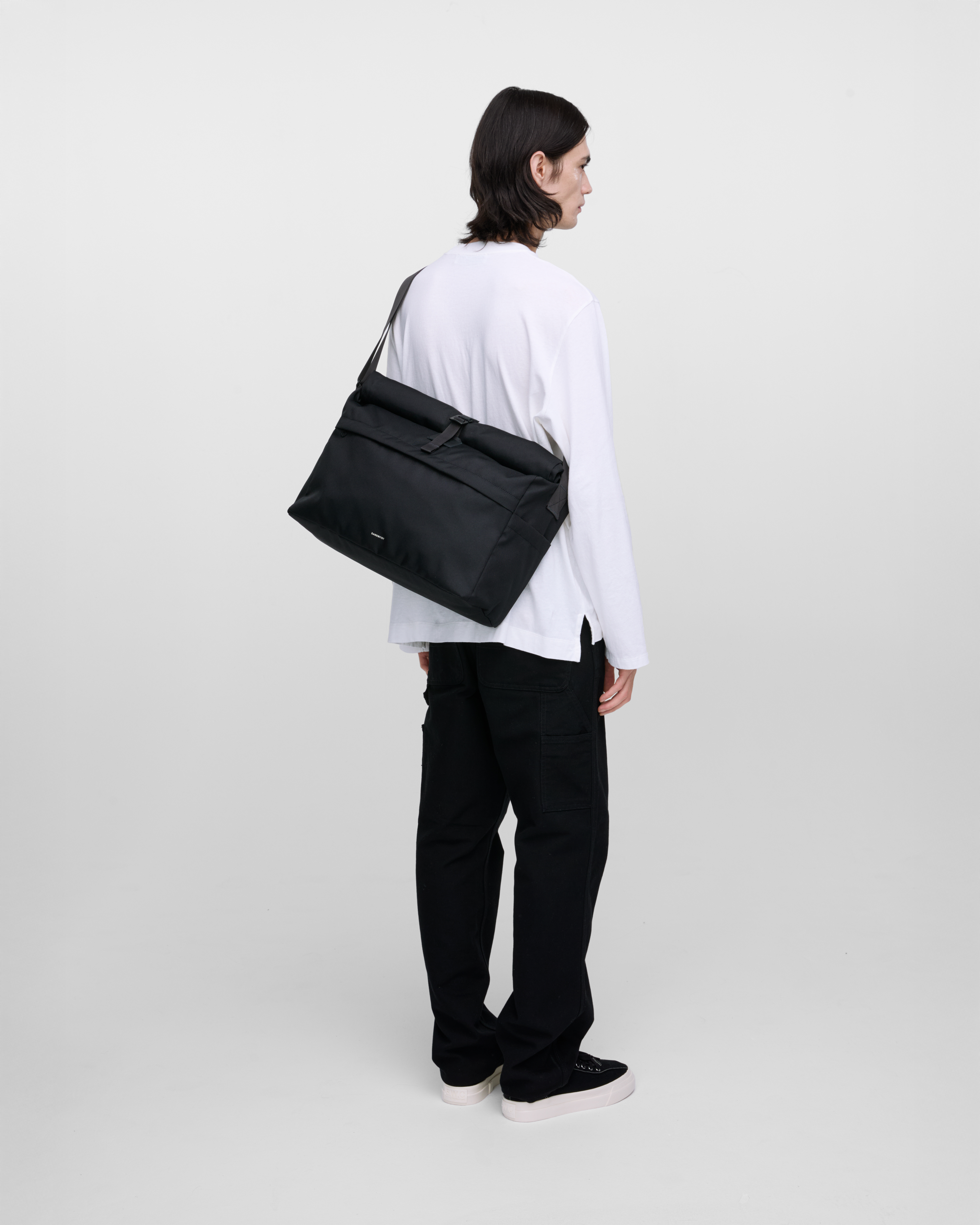 Male model wearing Sandqvist Icon Messenger Bag, black. Back view, wearing the bag on one shoulder crossbody.