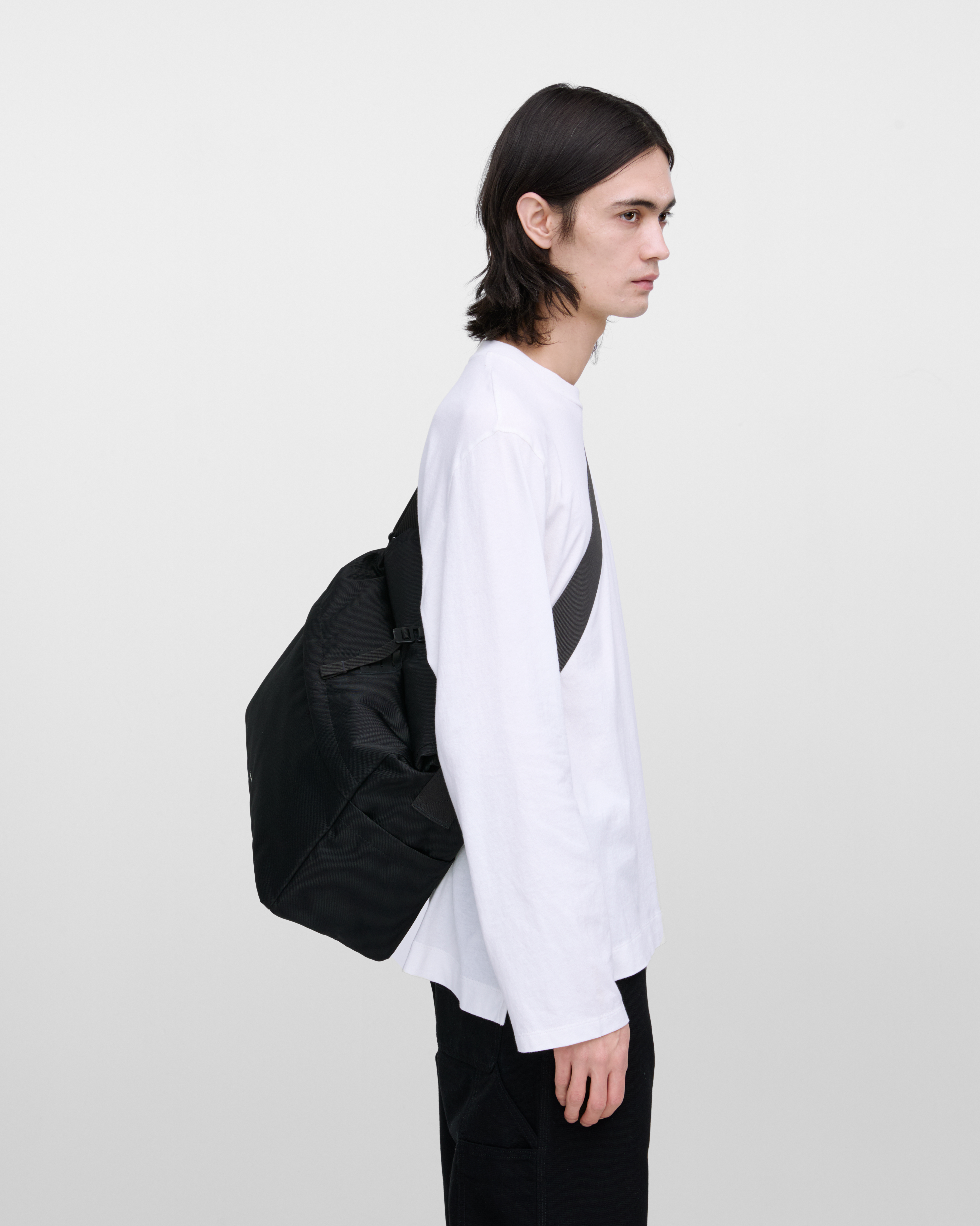 Male model wearing Sandqvist Icon Messenger Bag, black. Side view, wearing the bag on one shoulder crossbody.
