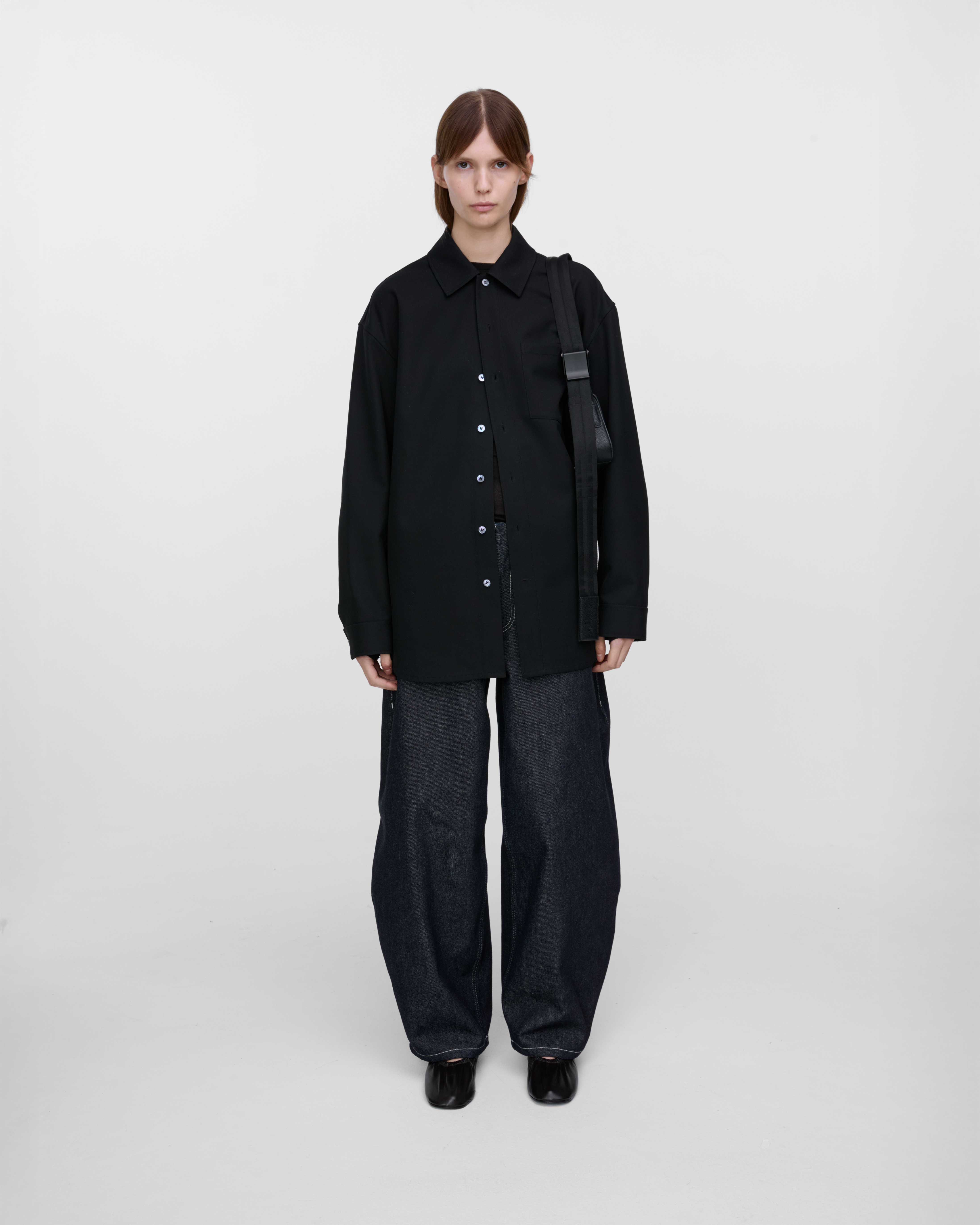 Female model carrying Sandqvist Agile Handle Crossbody Bag, black. Front view, carrying the bag over one shoulder.