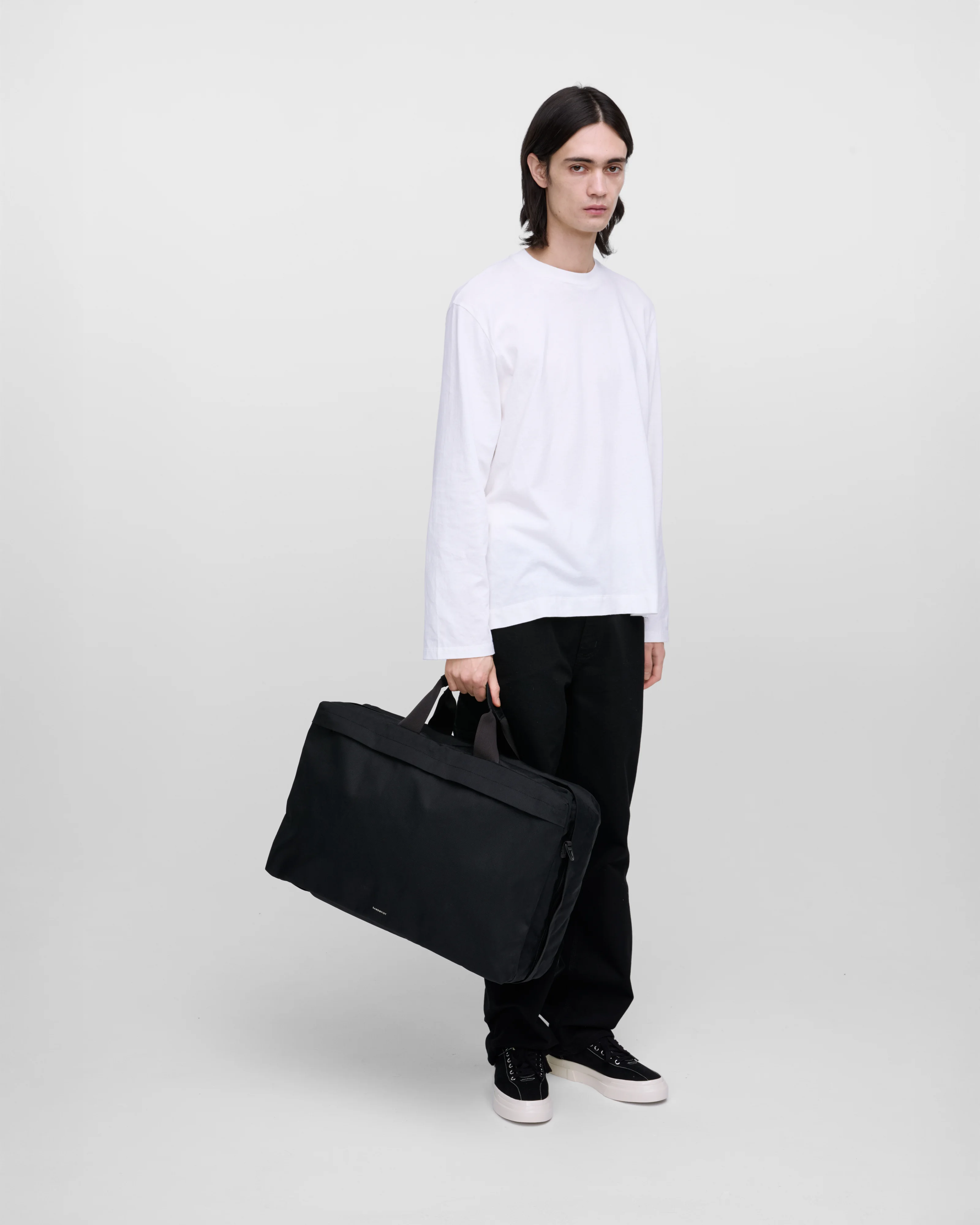 Male model holding Sandqvist GO 3-way bag L, black. Front view, holding the bag in one hand. 