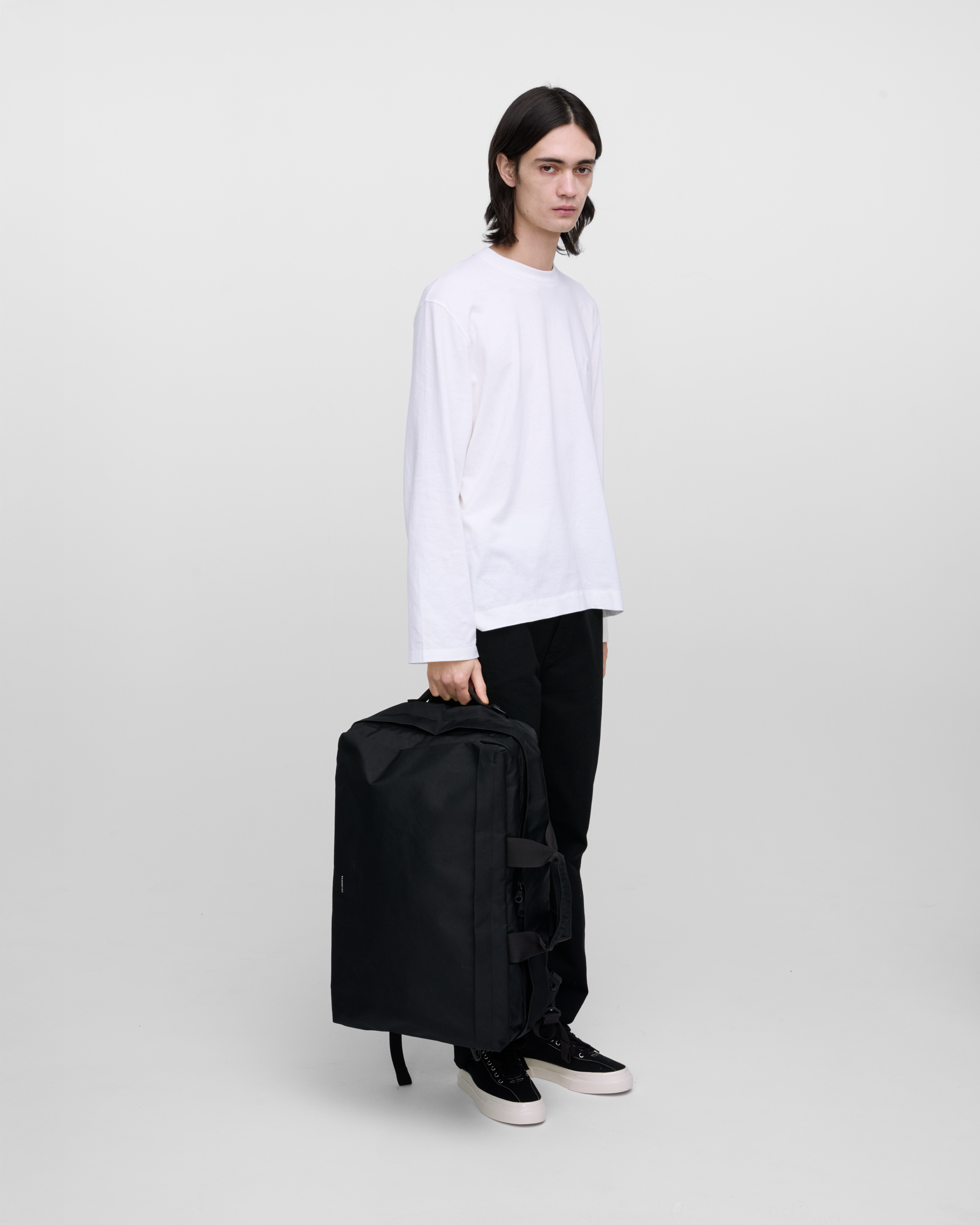 Male model holding Sandqvist GO 3-way bag L, black. Front view, holding the bag in one hand.
