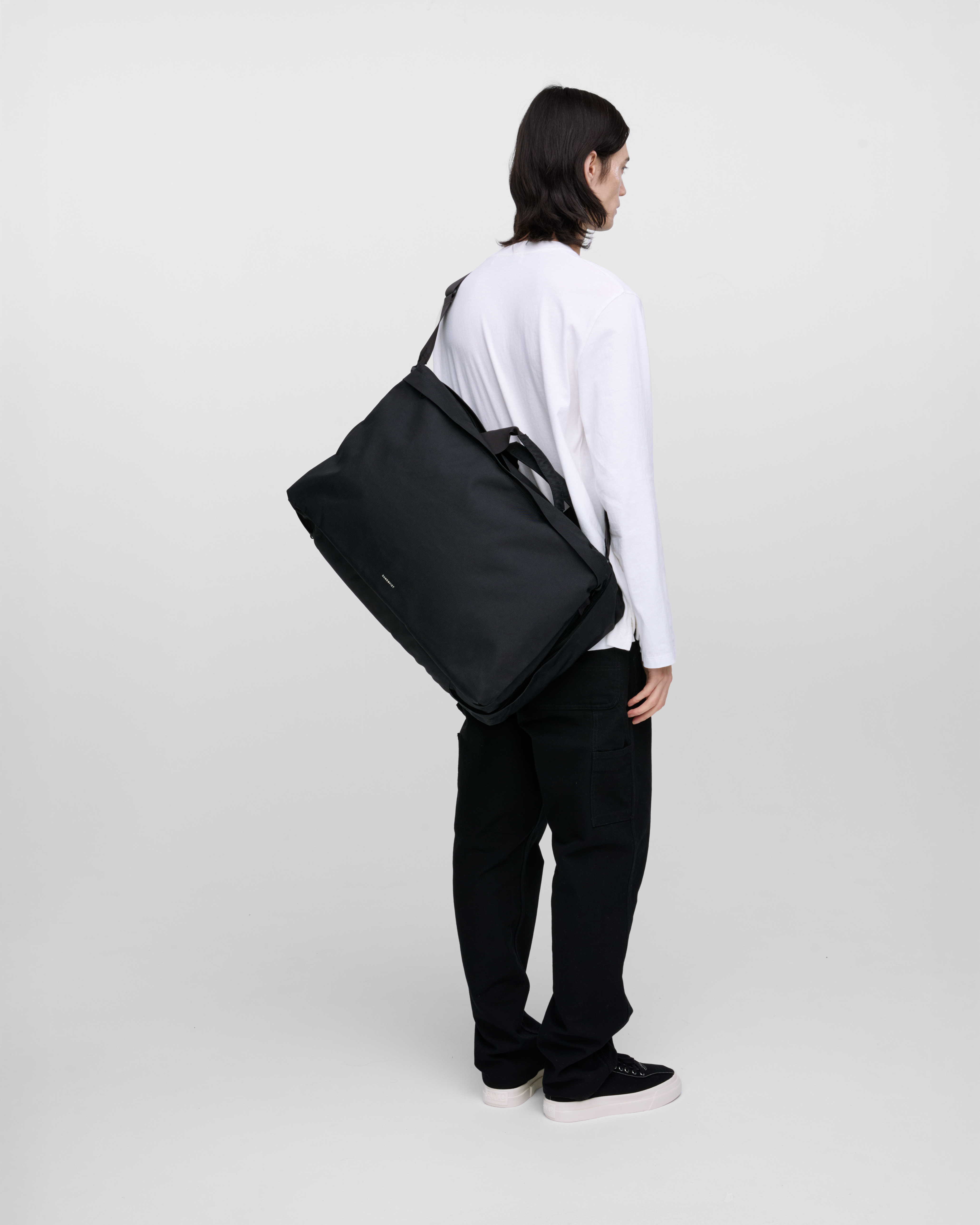 Male model wearing Sandqvist GO 3-way bag L, black. Back view, wearing the bag on one shoulder on the back.