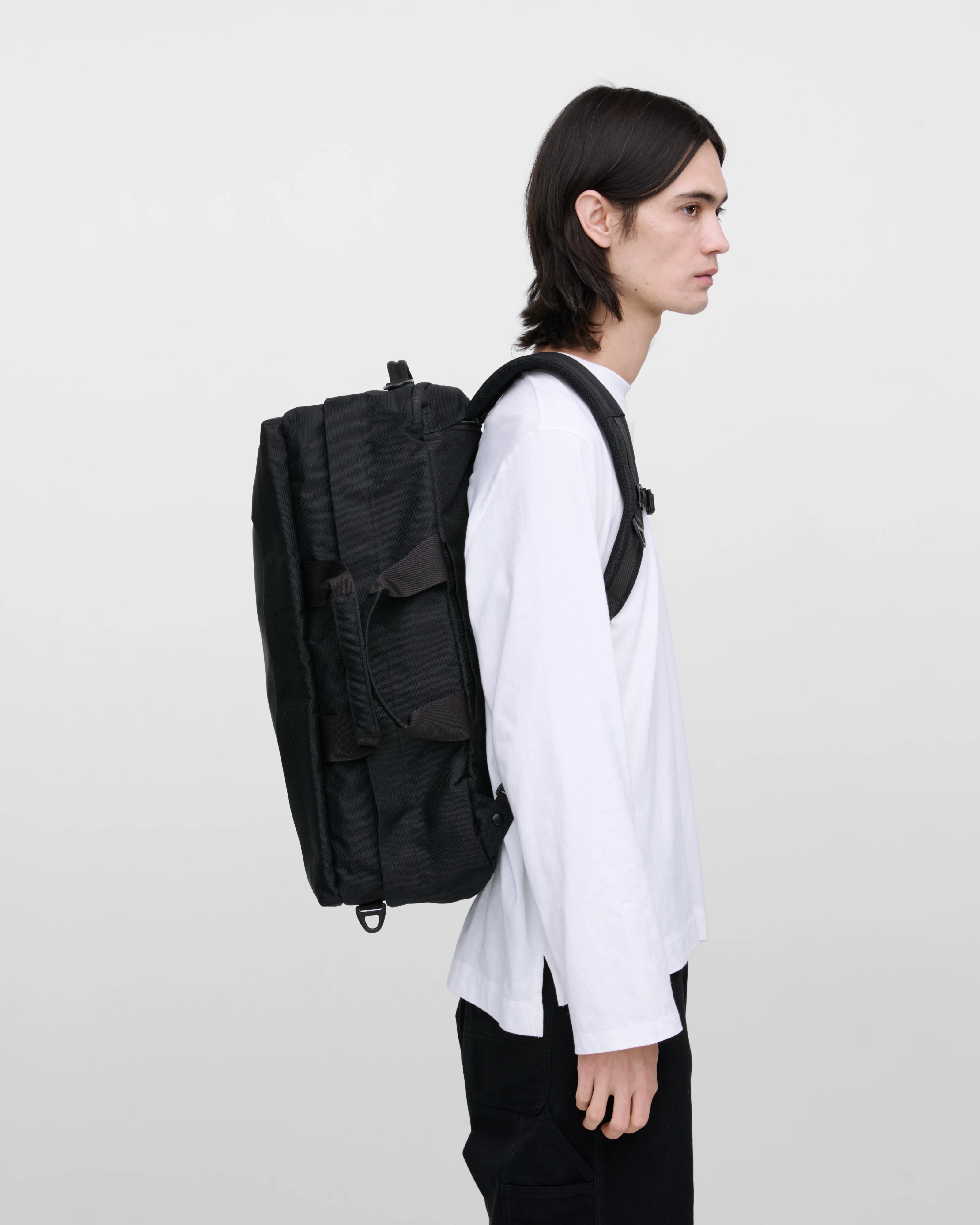 Male model wearing Sandqvist GO 3-way bag L, black. Side view, wearing the bag on the back.
