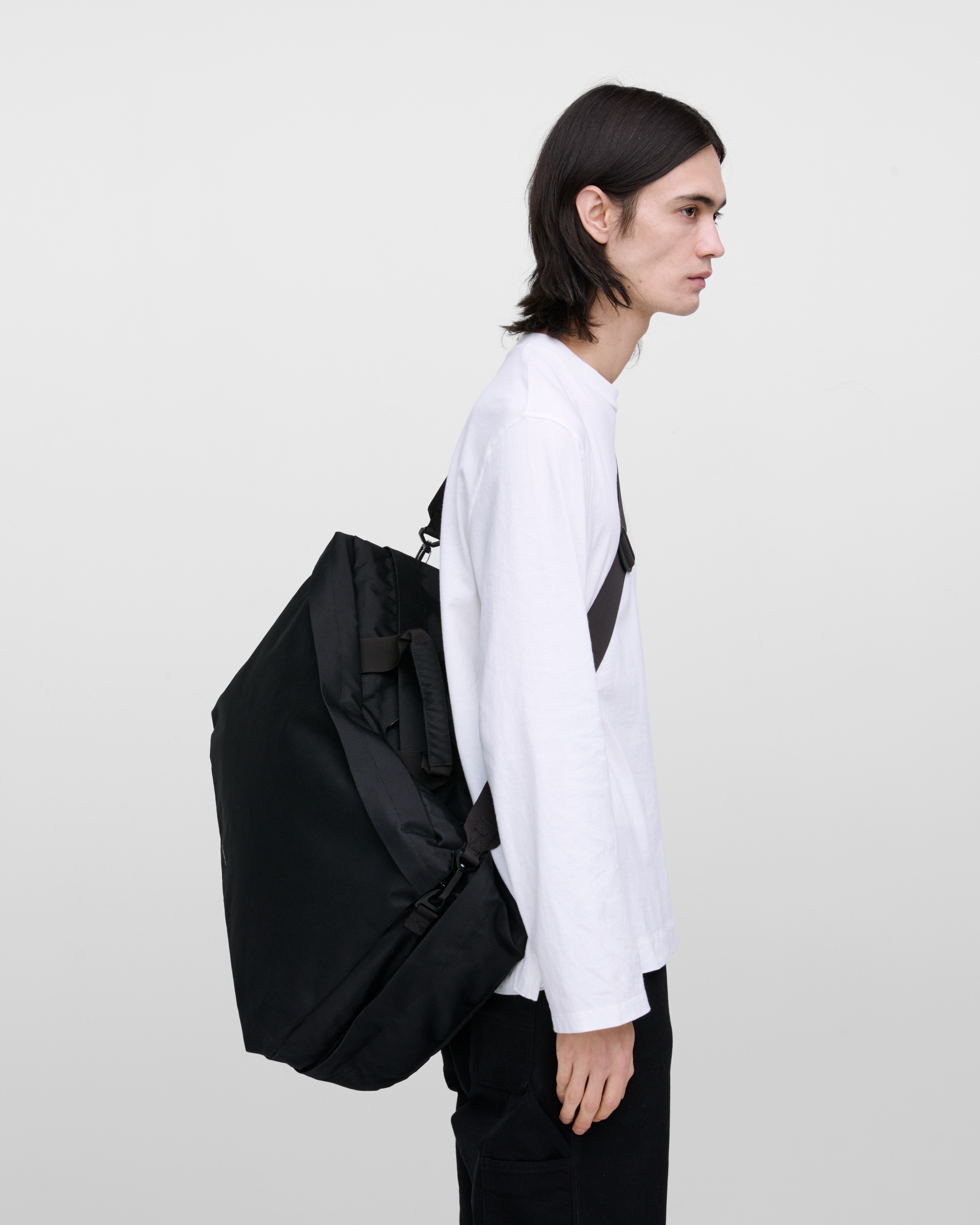 Male model wearing Sandqvist GO 3-way bag L, black. Side view, wearing the bag on one shoulder on the back.