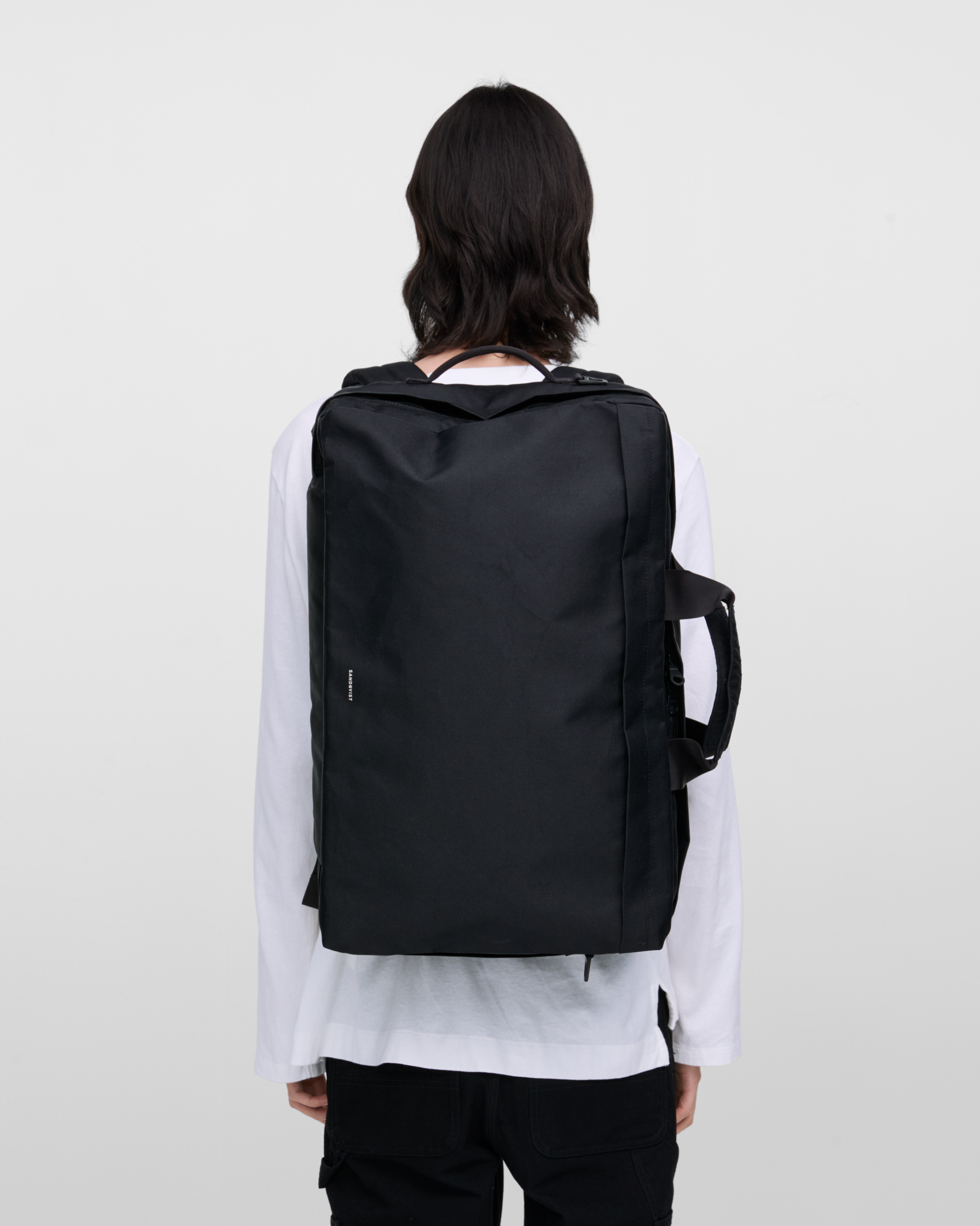 Male model wearing Sandqvist GO 3-way bag L, black. Back view, wearing the bag on the back.