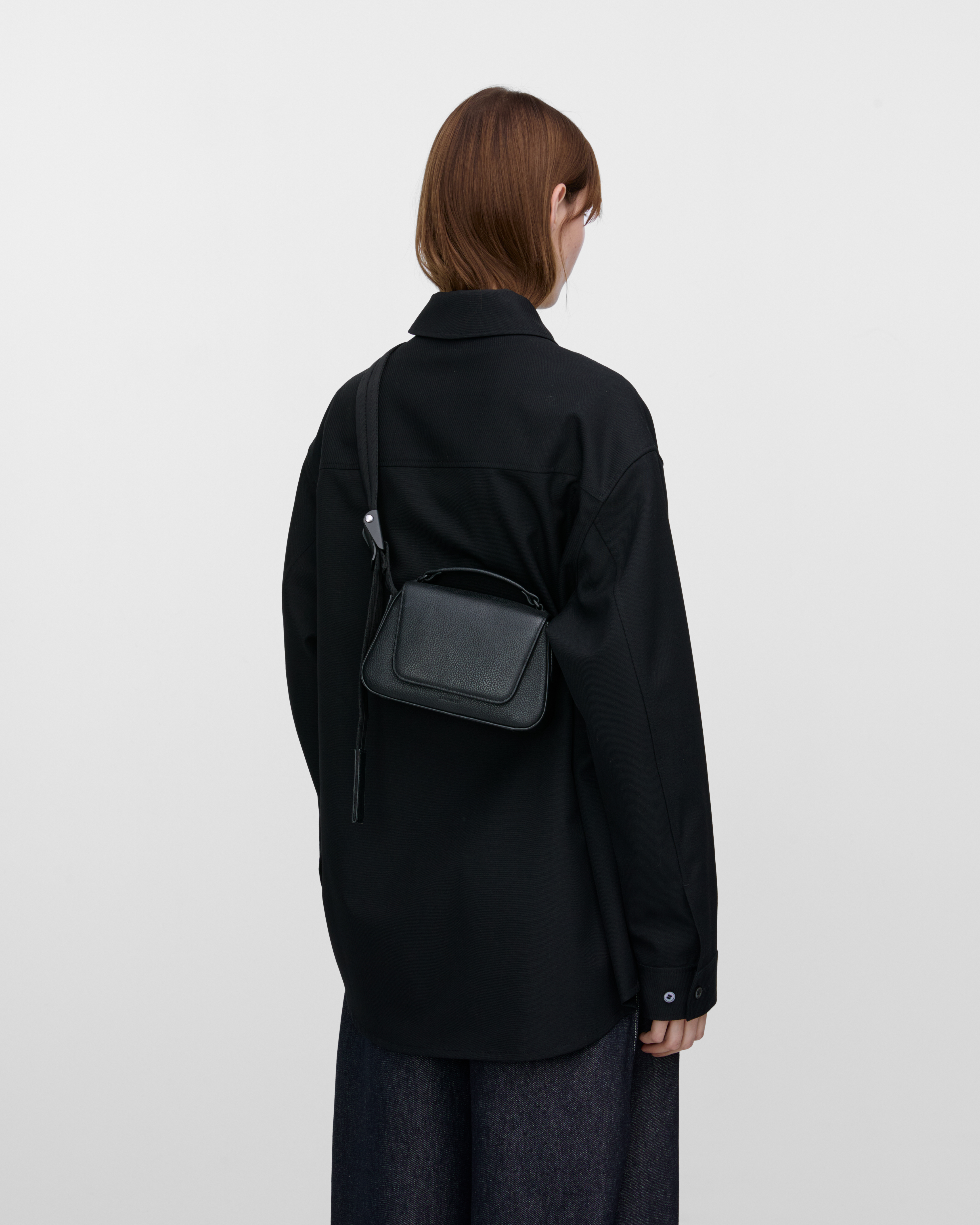 Female model wearing Sandqvist Agile Handle Crossbody Bag, black. Back view, wearing the bag on one shoulder crossbody.