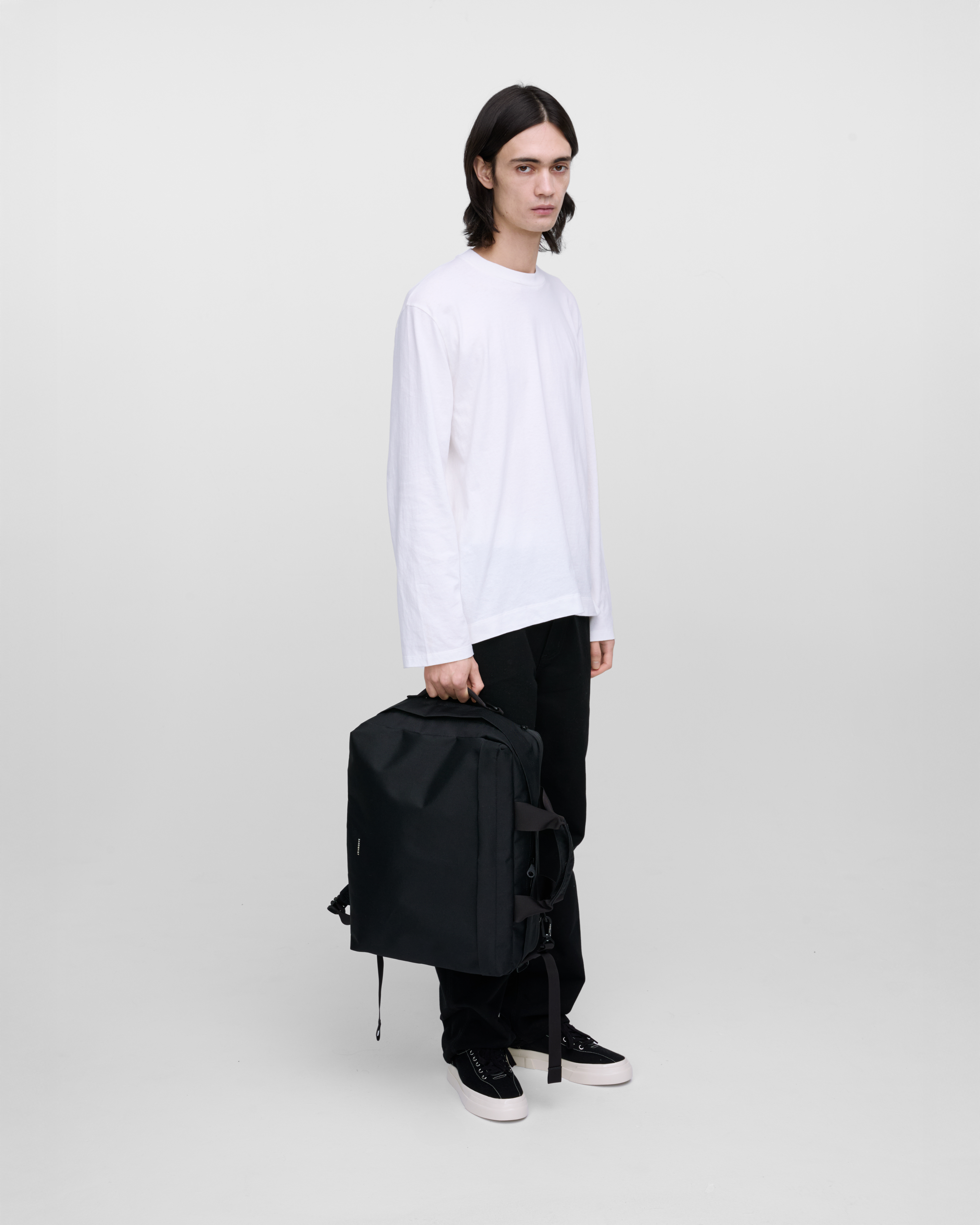 Male model holding Sandqvist GO 3-Way Bag M, black. Front view, holding the bag in one hand, in the side handle.