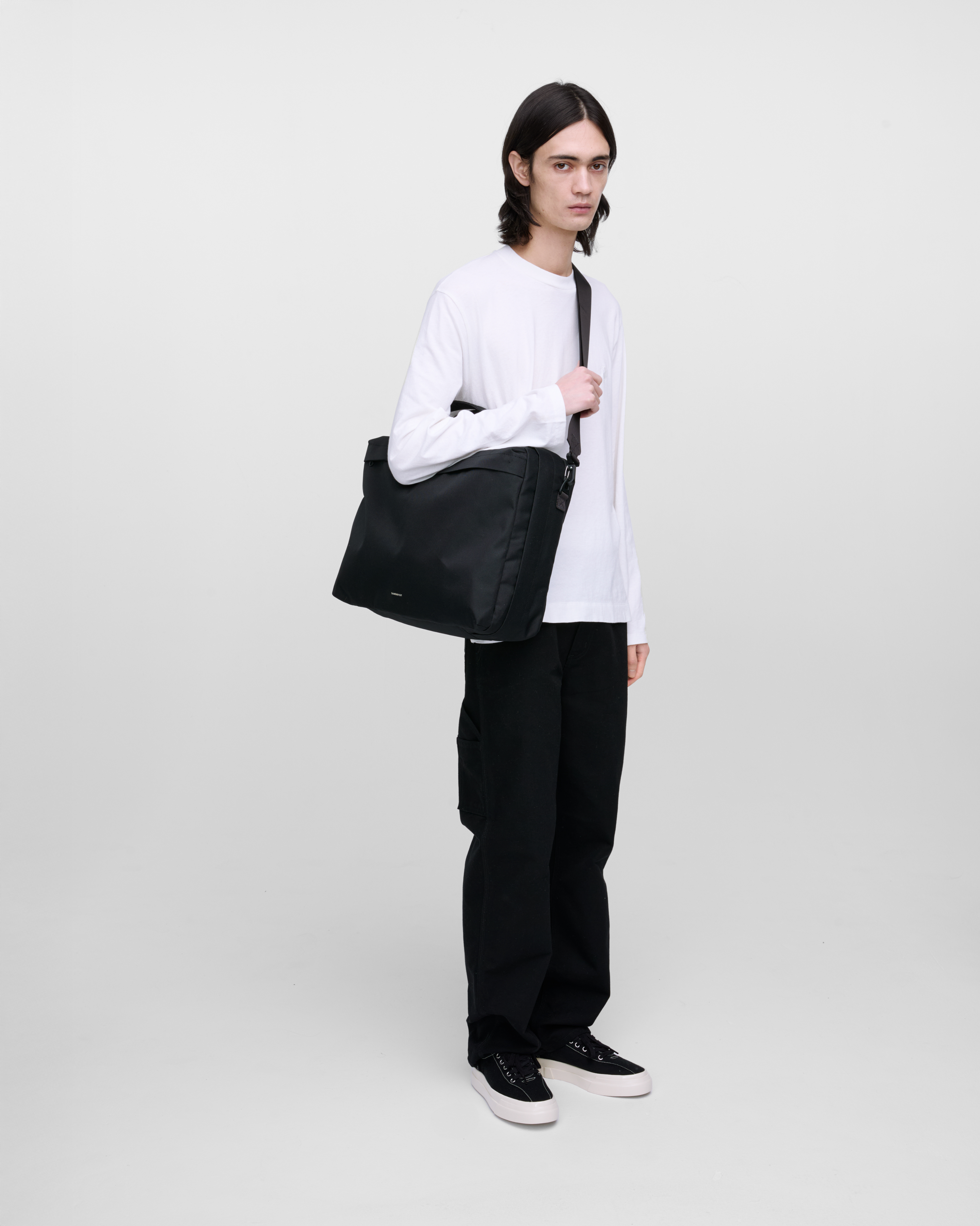 Male model wearing Sandqvist GO 3-Way Bag M, black. Front view, wearing the bag on one shoulder crossbody.