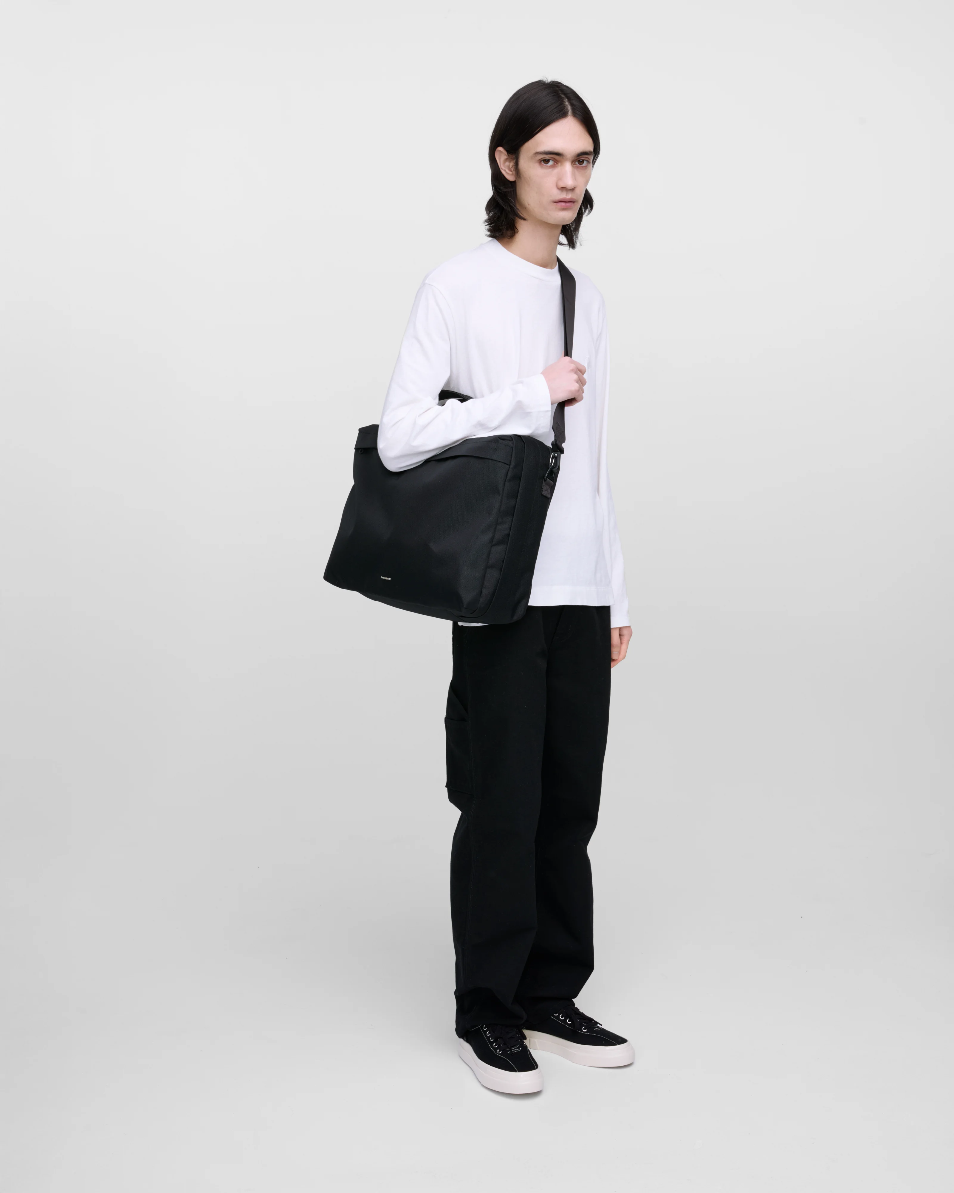 Male model wearing Sandqvist GO 3-Way Bag M, black. Front view, wearing the bag on one shoulder crossbody.