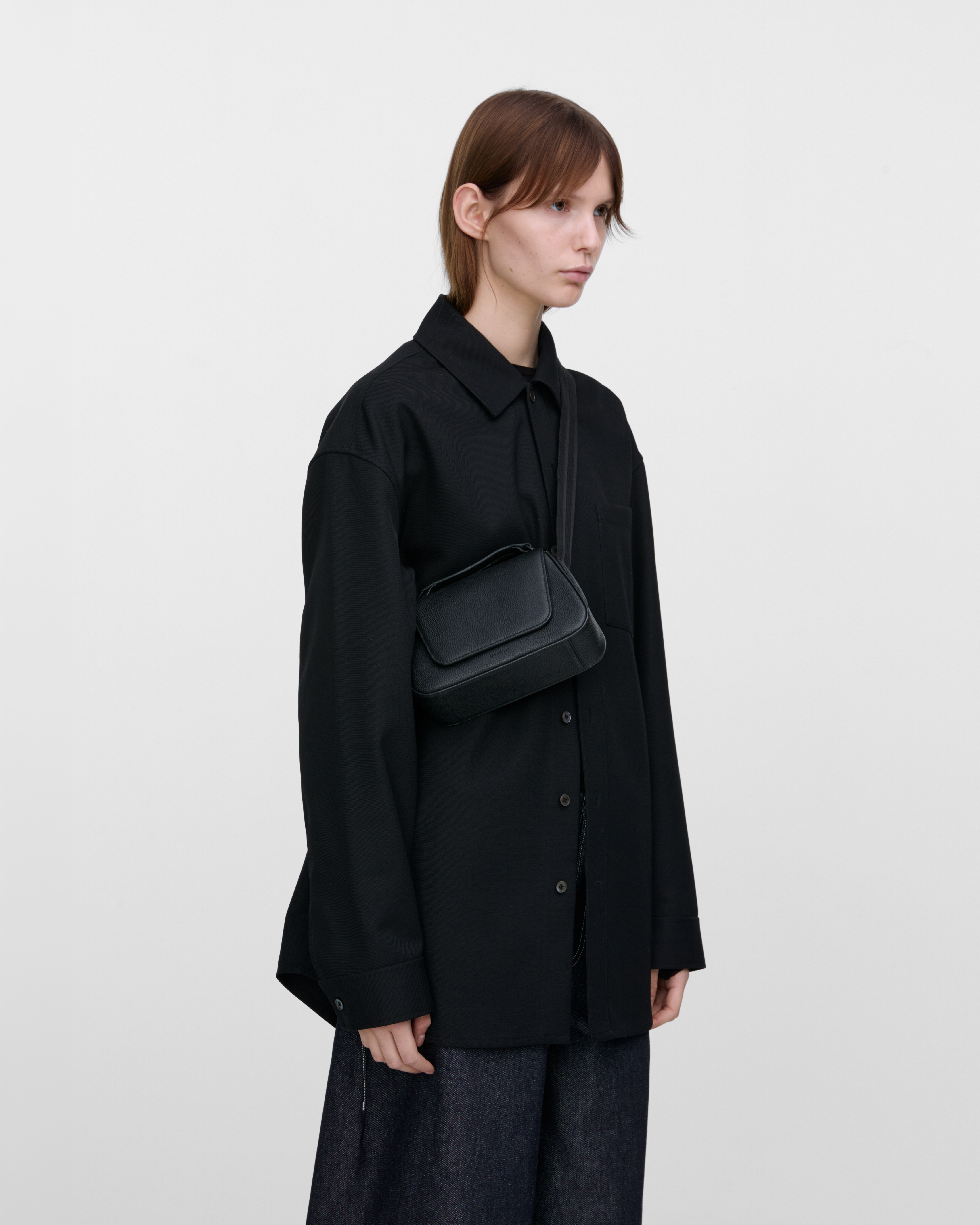 Female model wearing Sandqvist Agile Handle Crossbody Bag, black. Side view, wearing the bag on one shoulder crossbody.