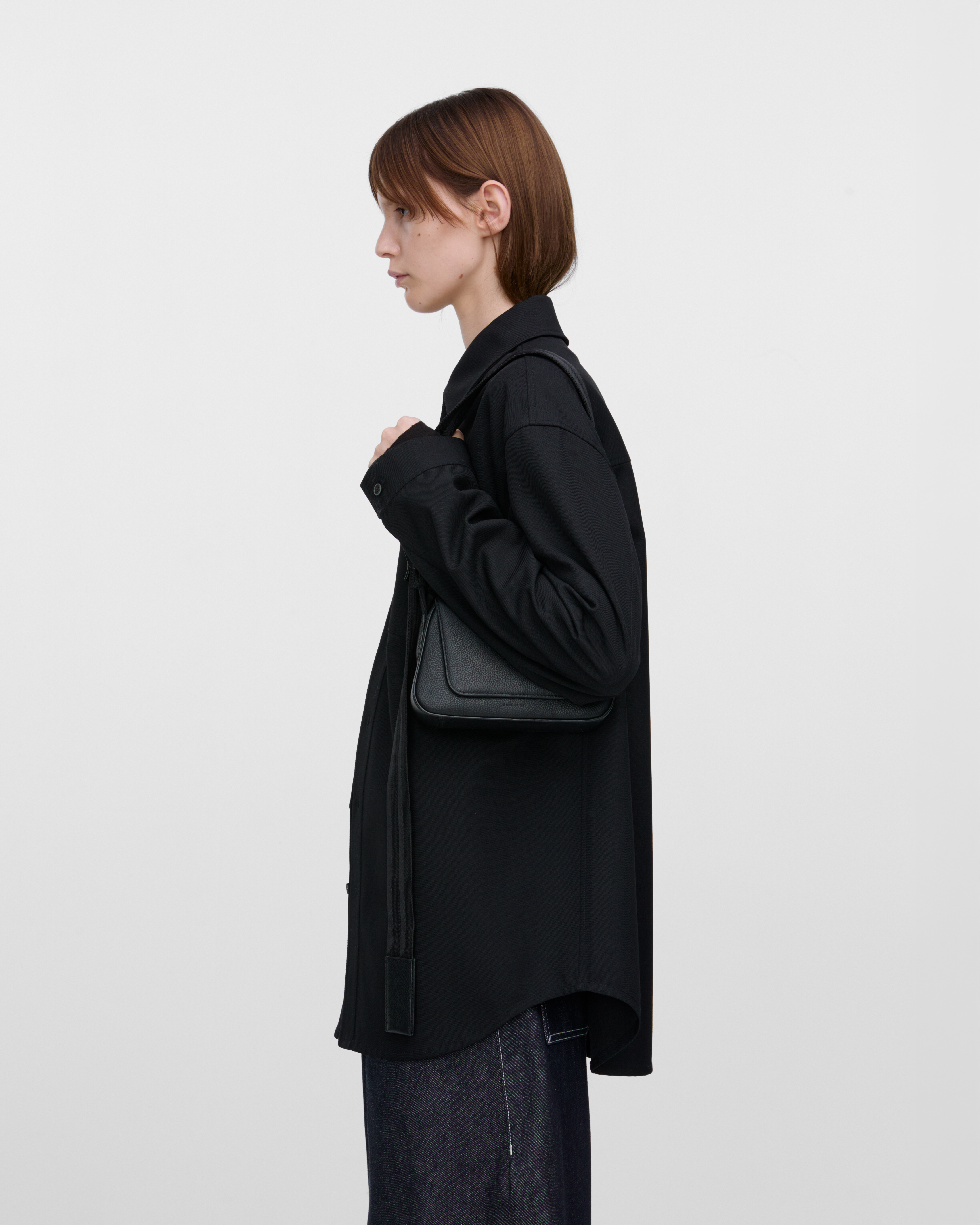 Female model wearing Sandqvist Agile Handle Crossbody Bag, black. Side view, wearing the bag on one shoulder.