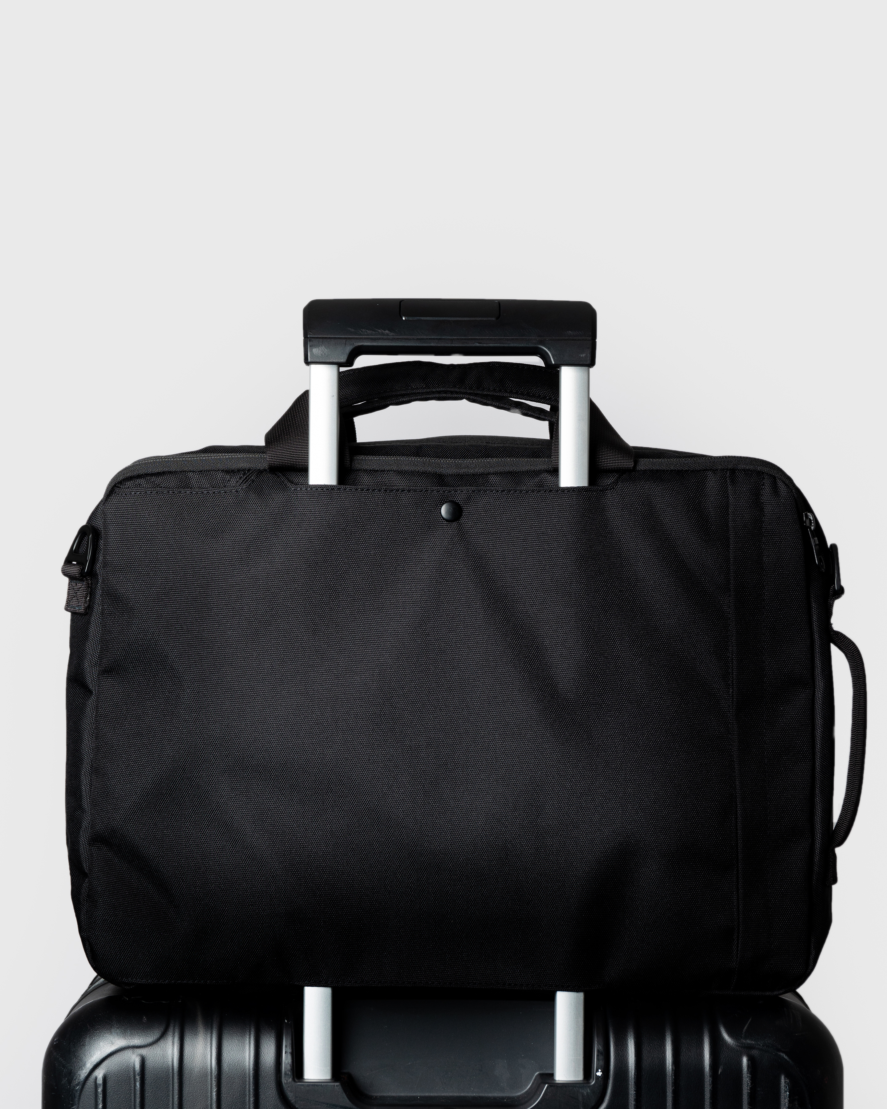 Sandqvist GO 3-Way Bag M, black. Back view, attached to a cabin bag with the trolley sleeve.