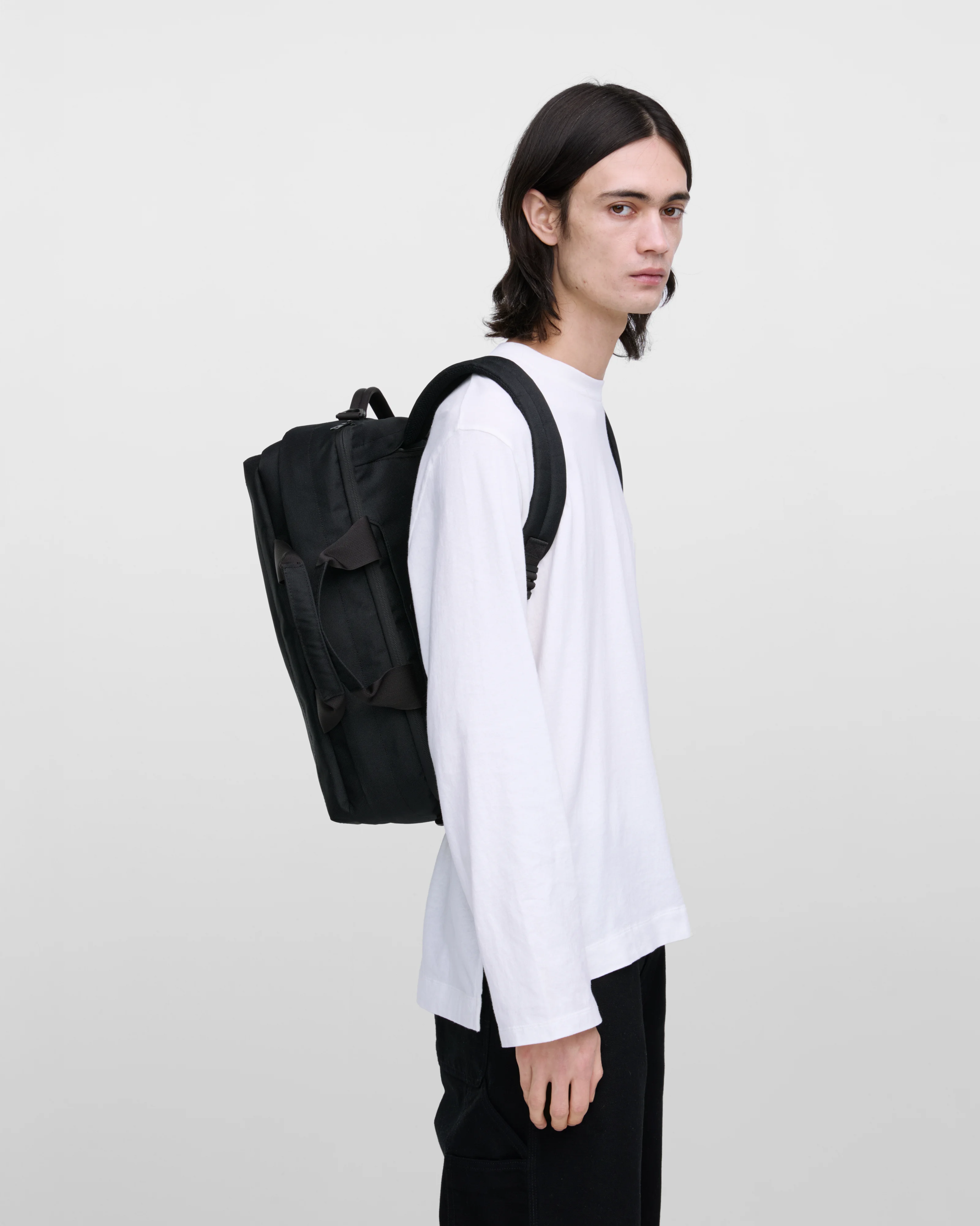 Male model wearing Sandqvist GO 3-Way Bag M, black. Side view, wearing the bag on the back.