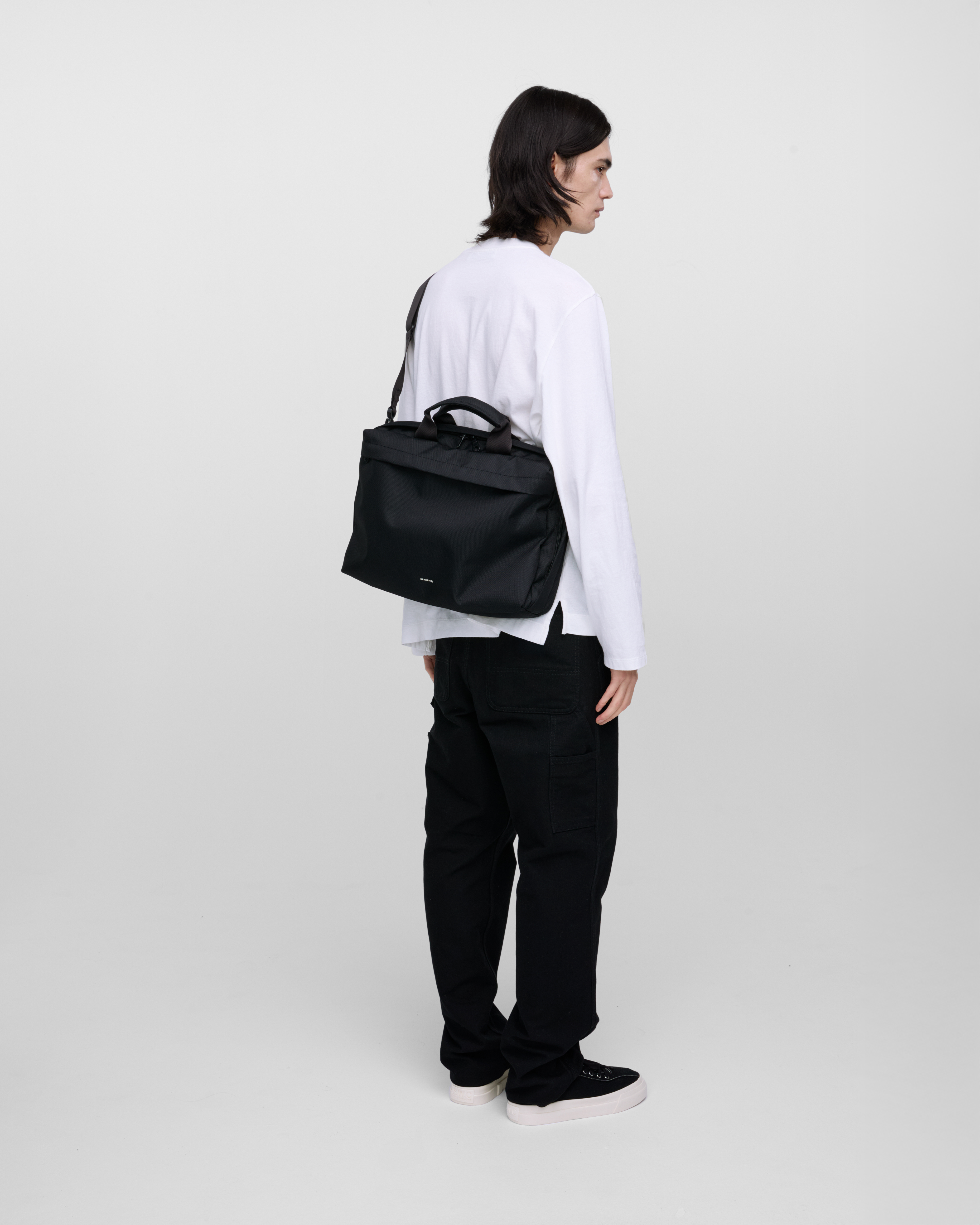 Male model wearing GO Briefcase, black. Back view, wearing the bag on one shoulder crossbody.