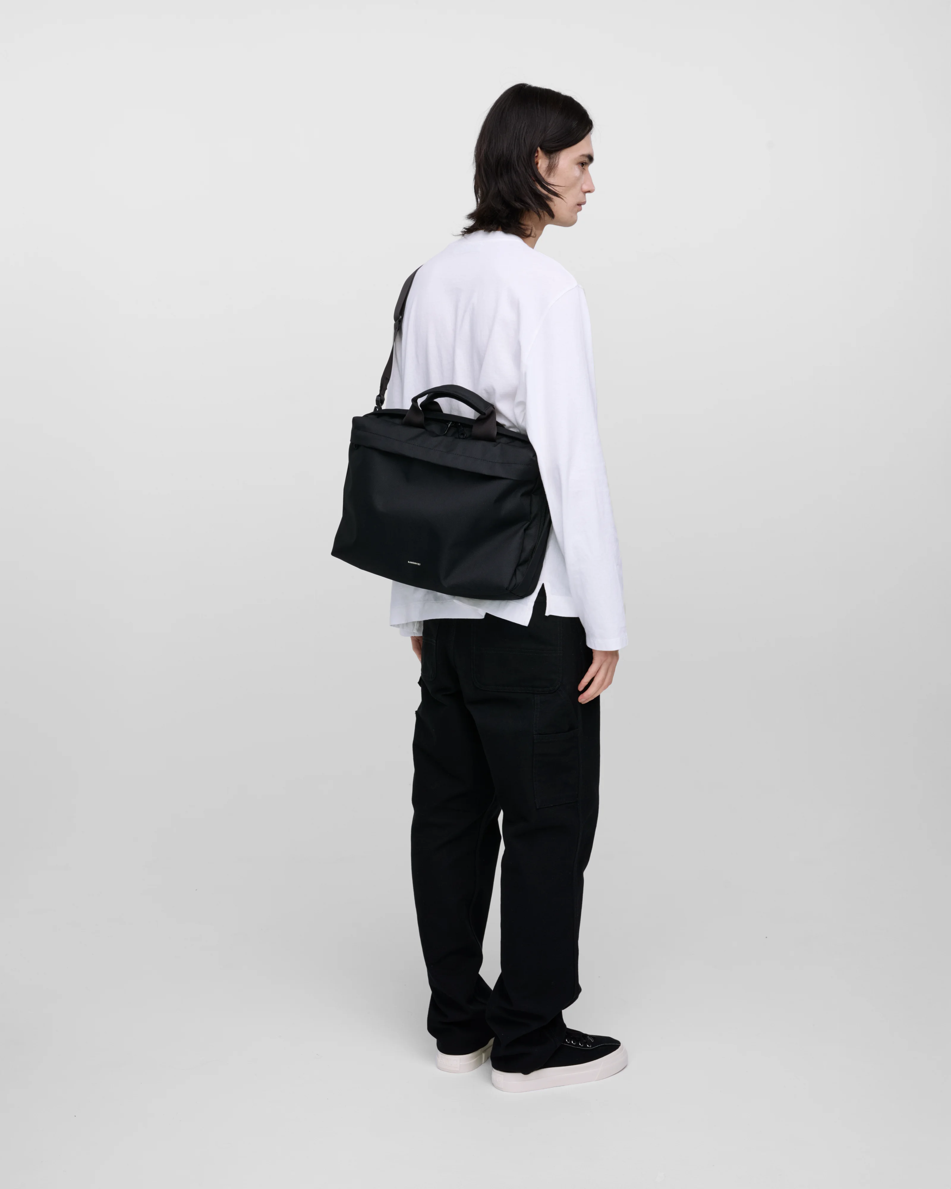 Male model wearing GO Briefcase, black. Back view, wearing the bag on one shoulder crossbody.