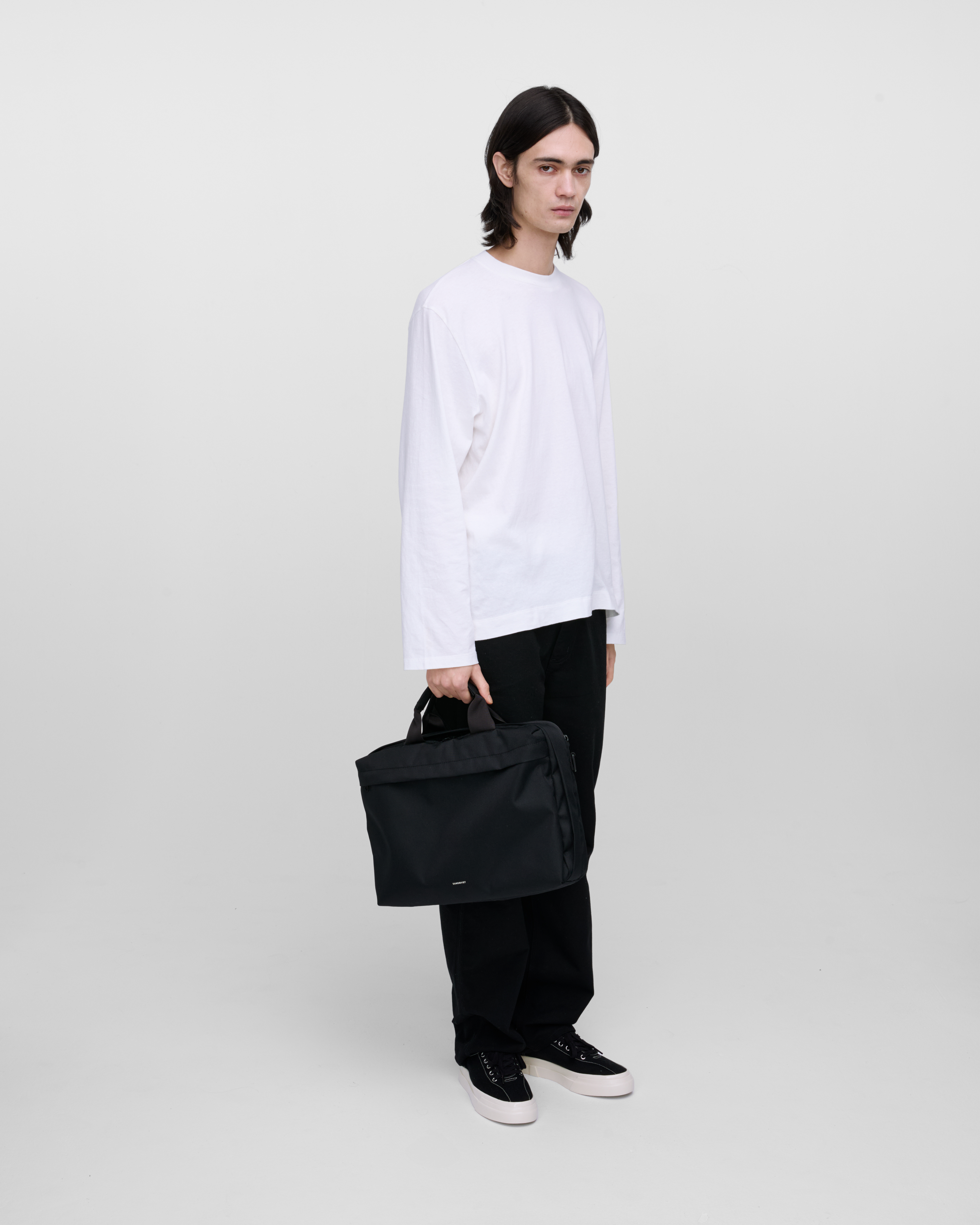 Male model holding GO Briefcase, black. Front view, holding the bag in one hand.