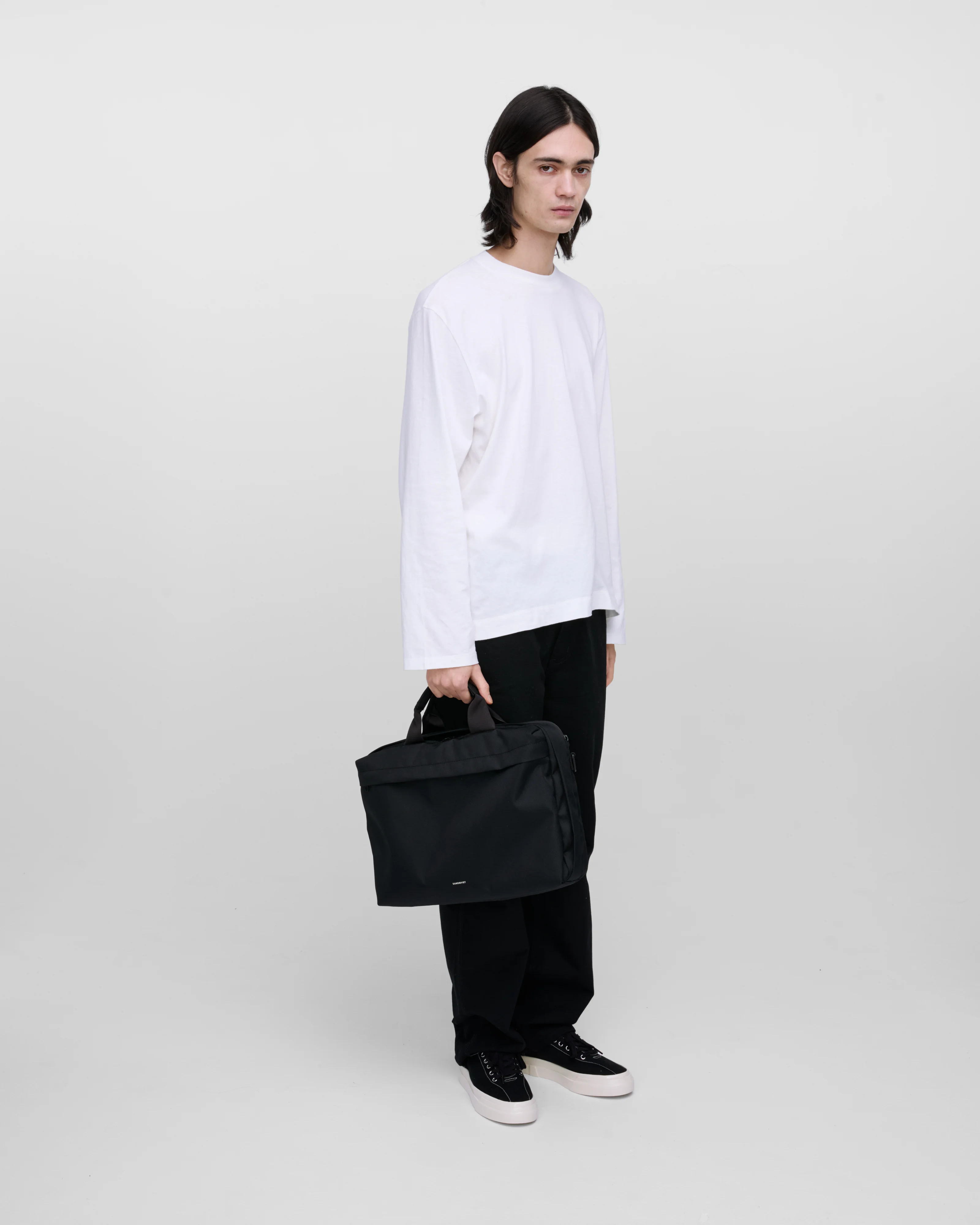 Male model holding GO Briefcase, black. Front view, holding the bag in one hand.