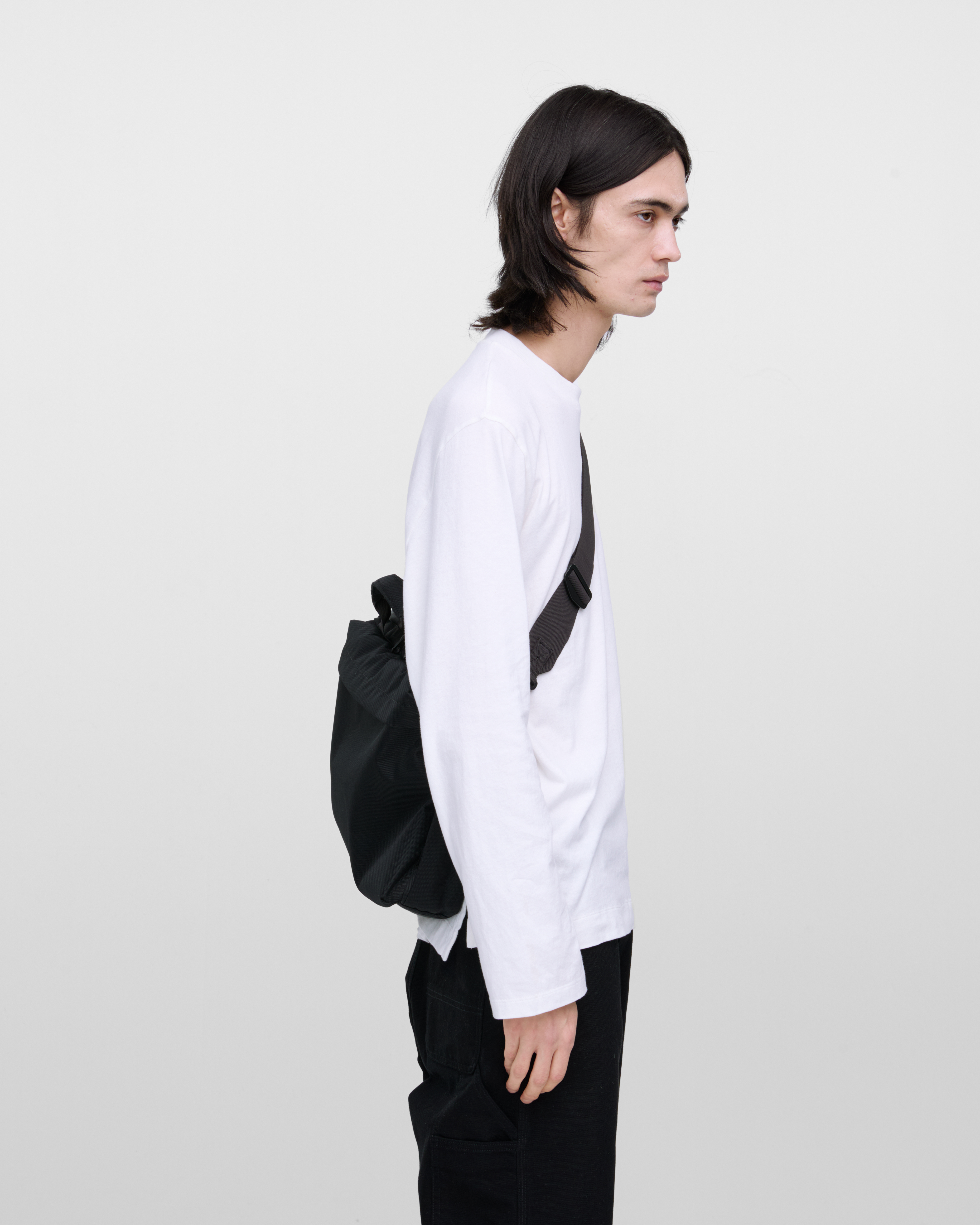 Male model wearing GO Briefcase, black. Side view, wearing the bag on one shoulder crossbody.