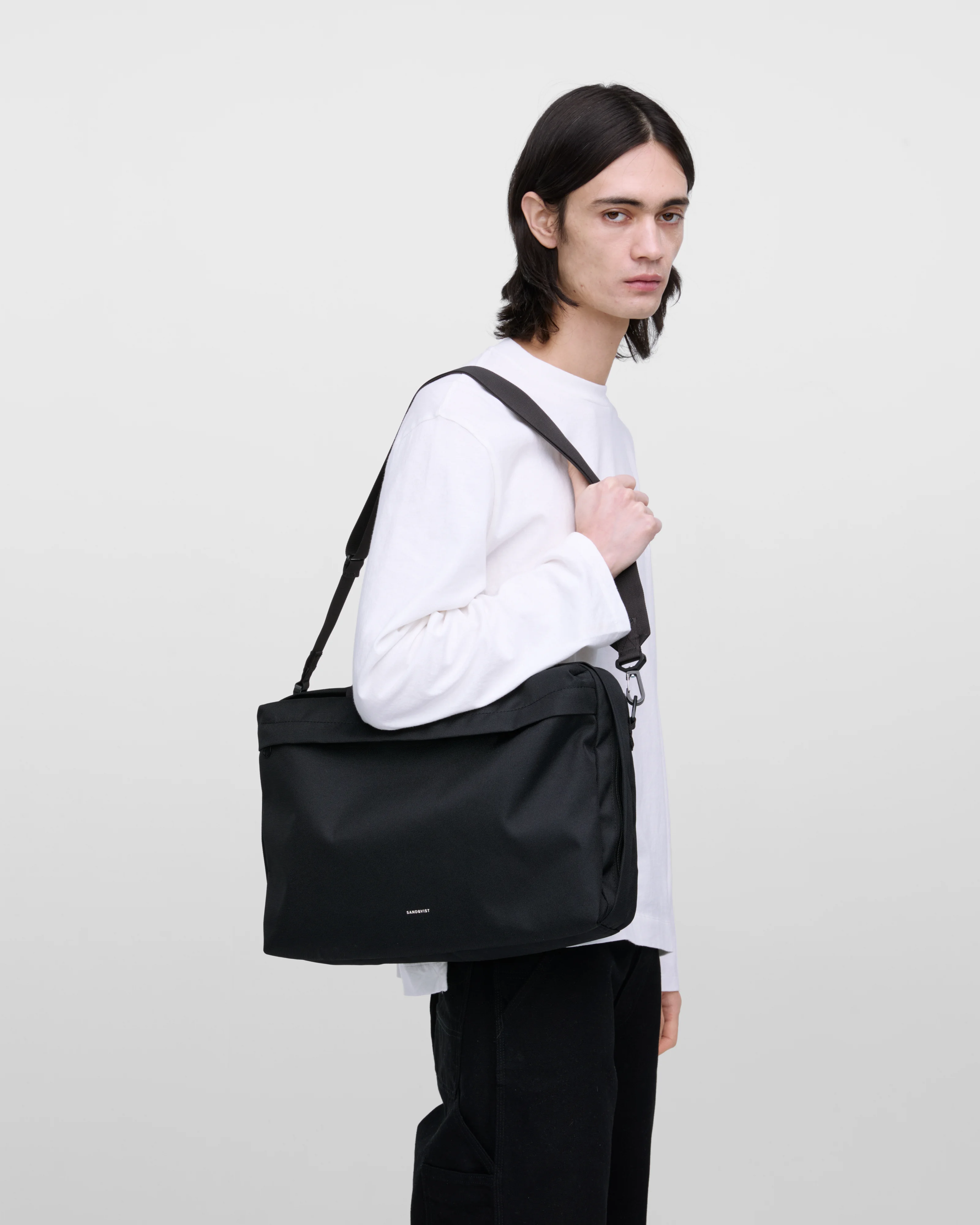 Male model wearing GO Briefcase, black. Side view, wearing the bag on one shoulder.