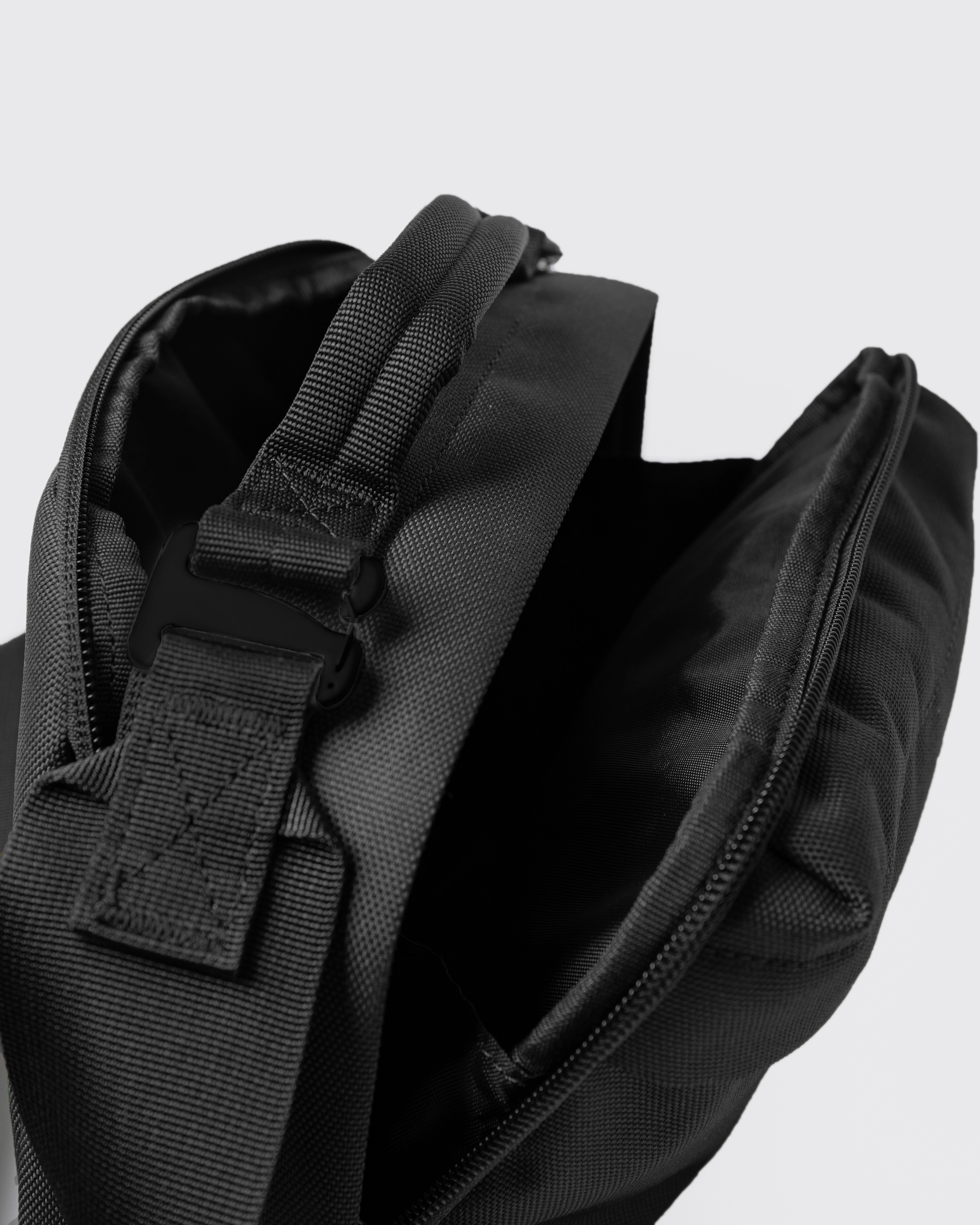 Sandqvist GO Shoulder Bag, black. Close-up of handle with a buckle and two compartments with zippers.