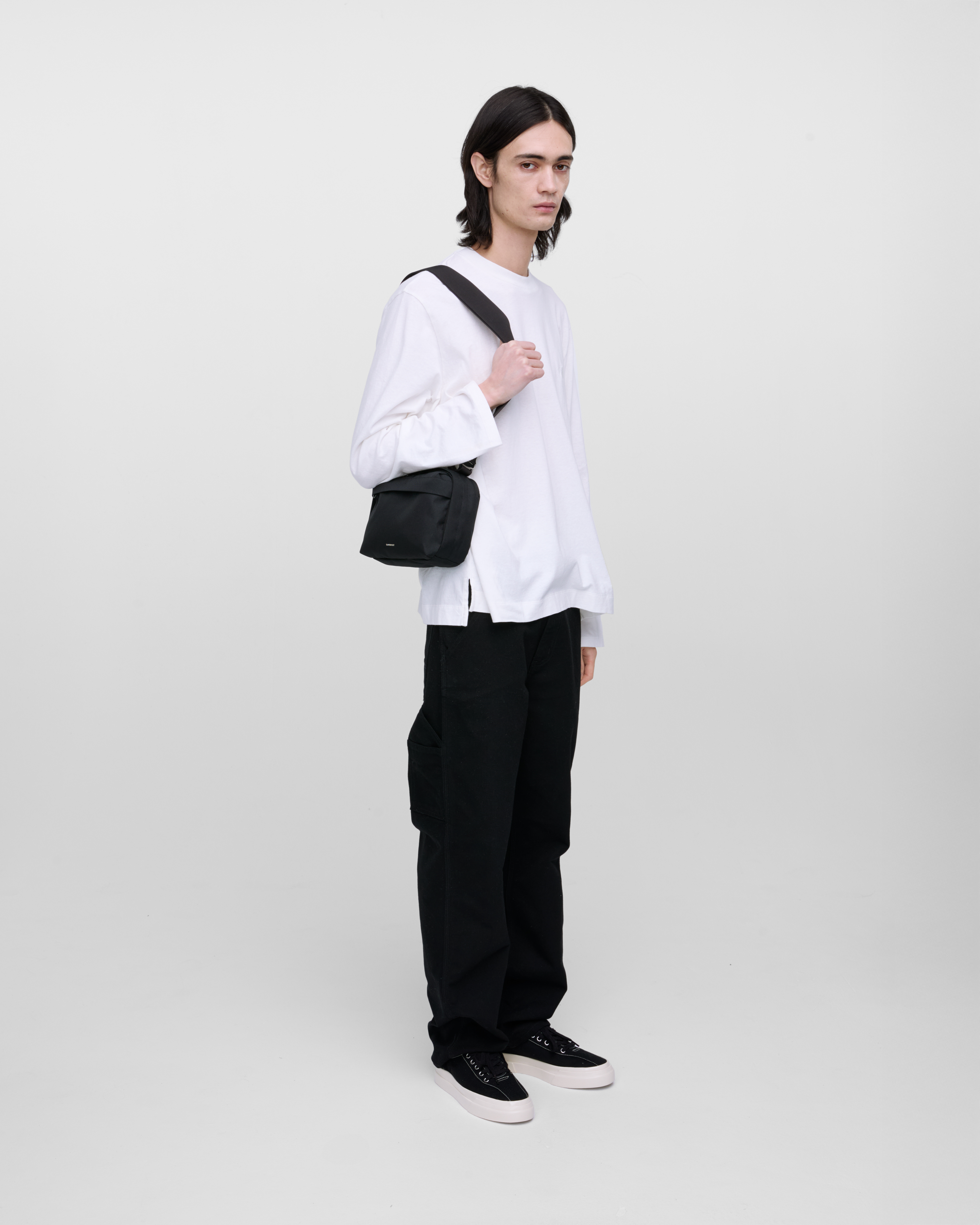 Male model wearing Sandqvist GO Shoulder Bag, black. Front view, wearing the bag on one shoulder.