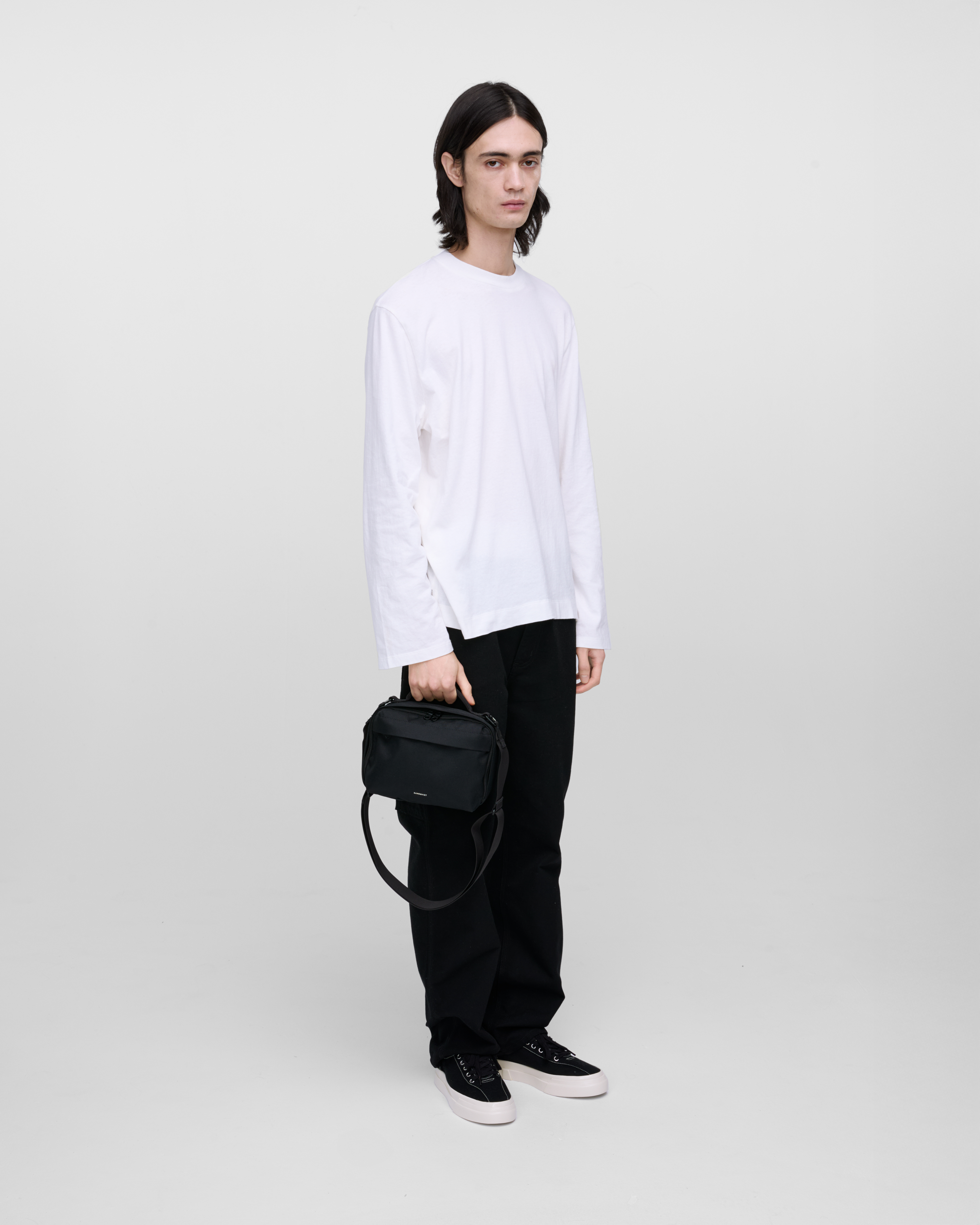 Male model holding Sandqvist GO Shoulder Bag, black. Front view, holding the bag in one hand.