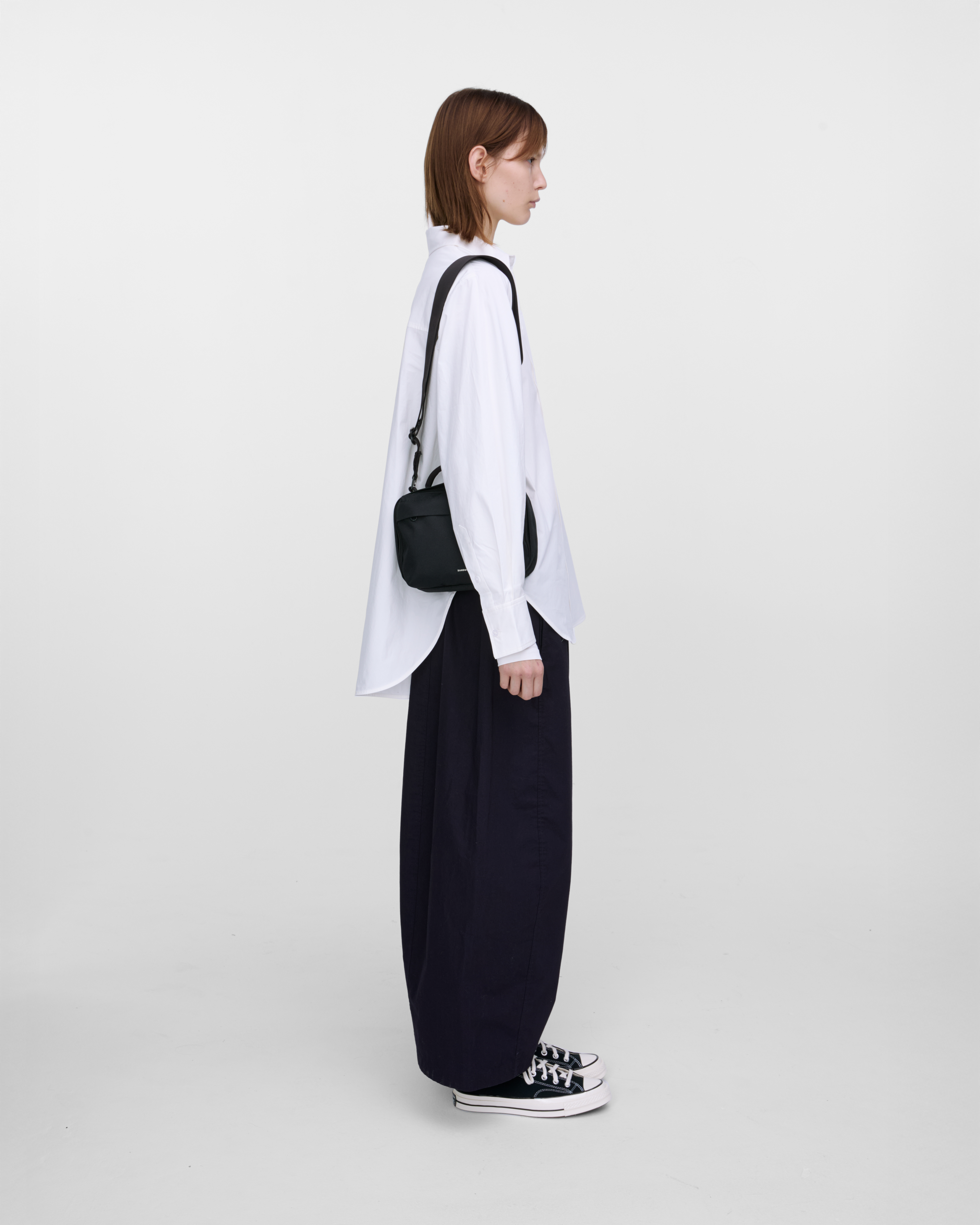 Female model wearing Sandqvist GO Shoulder Bag, black. Side view, wearing the bag on one shoulder.