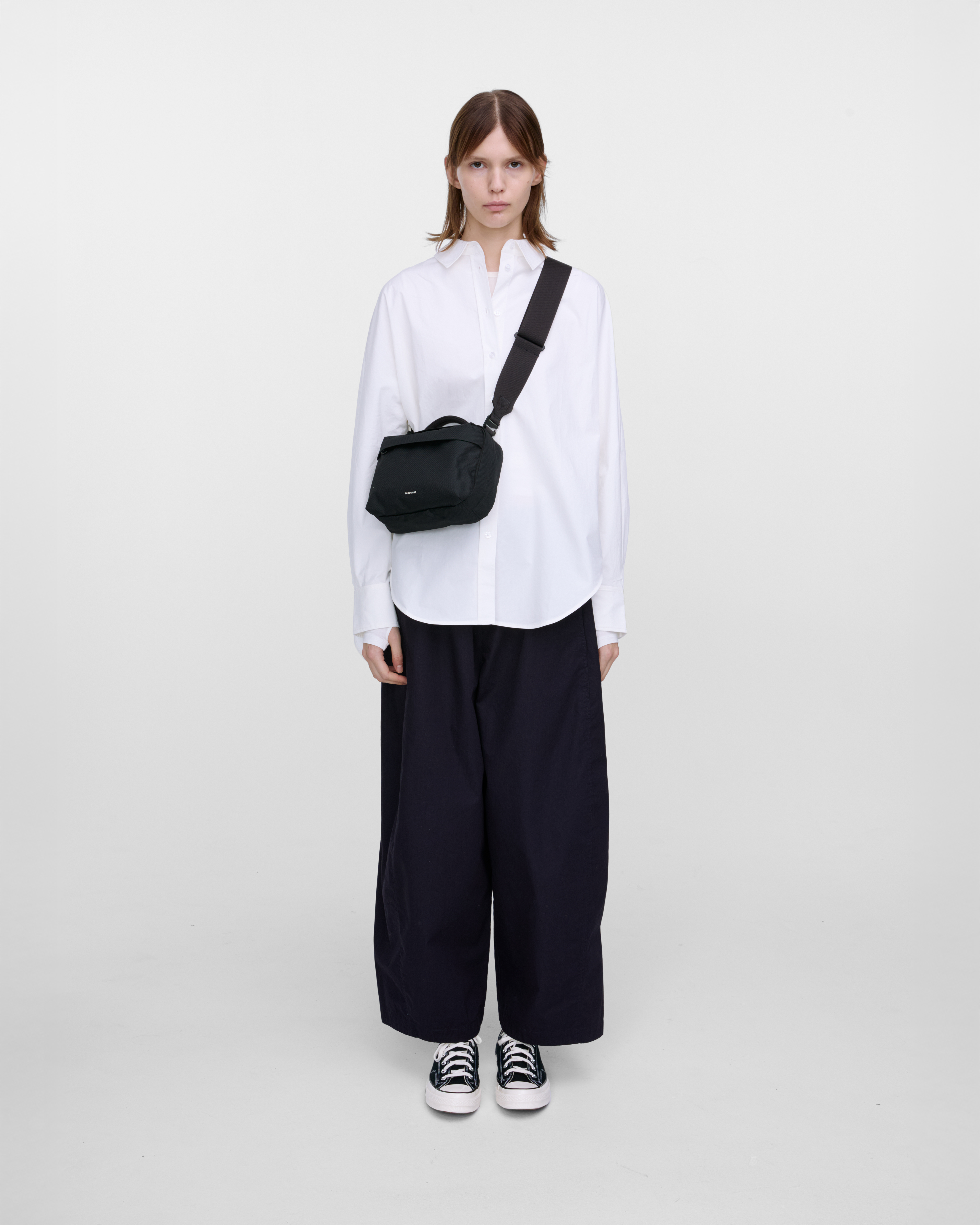 Female model wearing Sandqvist GO Shoulder Bag, black. Front view, wearing the bag on one shoulder crossbody.
