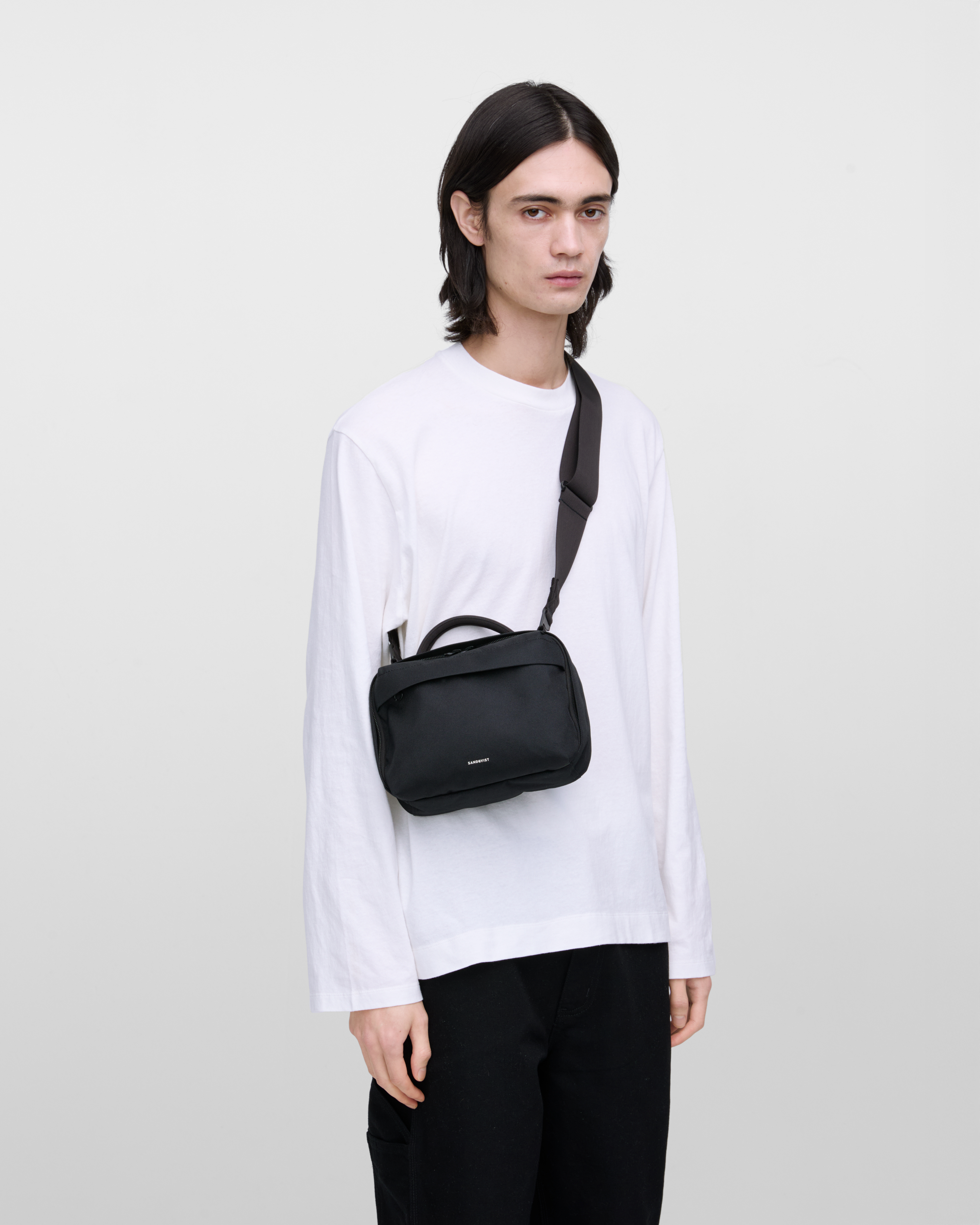 Male model wearing Sandqvist GO Shoulder Bag, black. Front view, wearing the bag on one shoulder crossbody.