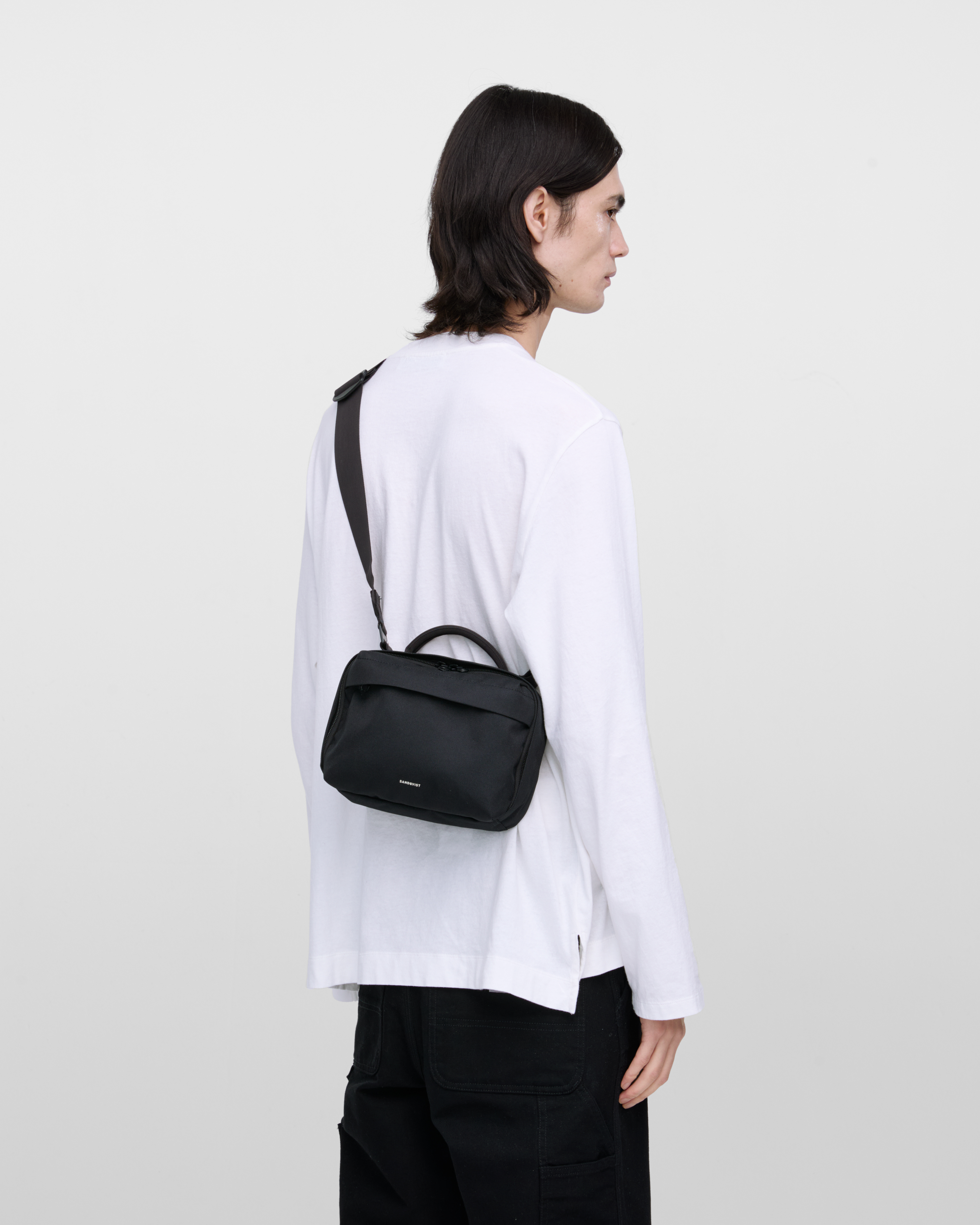 Male model wearing Sandqvist GO Shoulder Bag, black. Back view, wearing the bag on one shoulder crossbody.