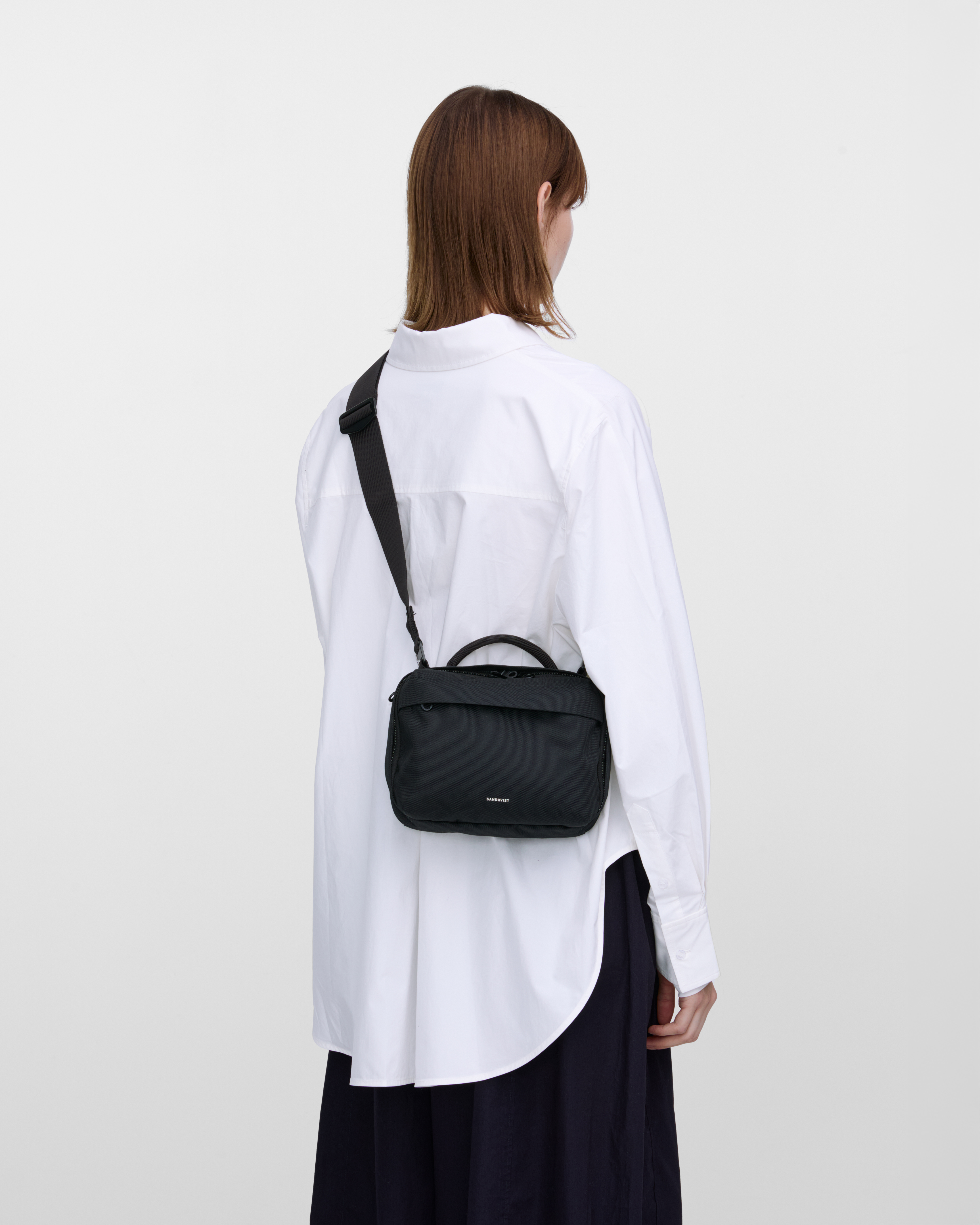 Female model wearing Sandqvist GO Shoulder Bag, black. Back view, wearing the bag on one shoulder crossbody.