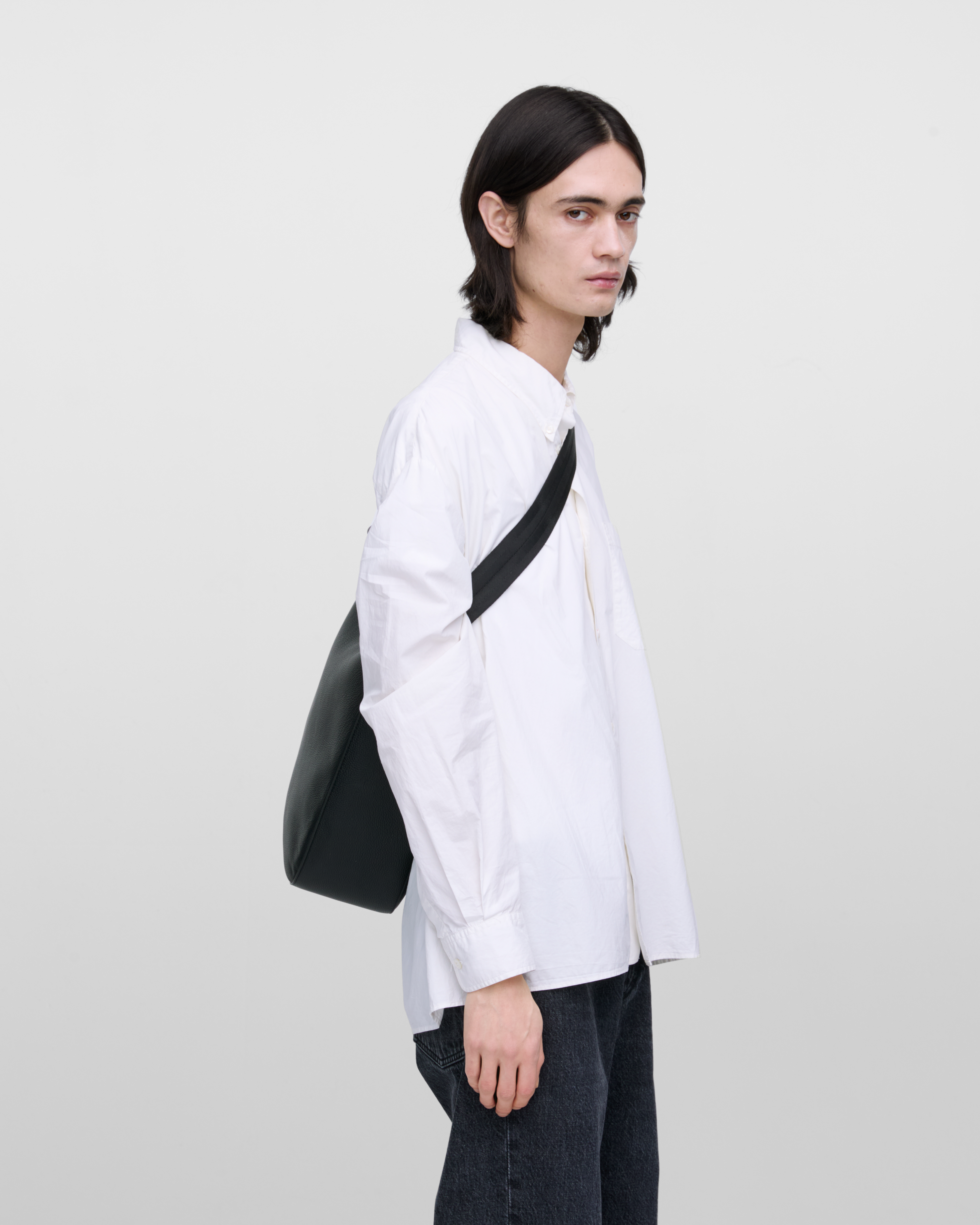 Male model wearing Sandqvist Agile Hobo Tote Bag, black. Side view, wearing the bag on one shoulder crossbody.