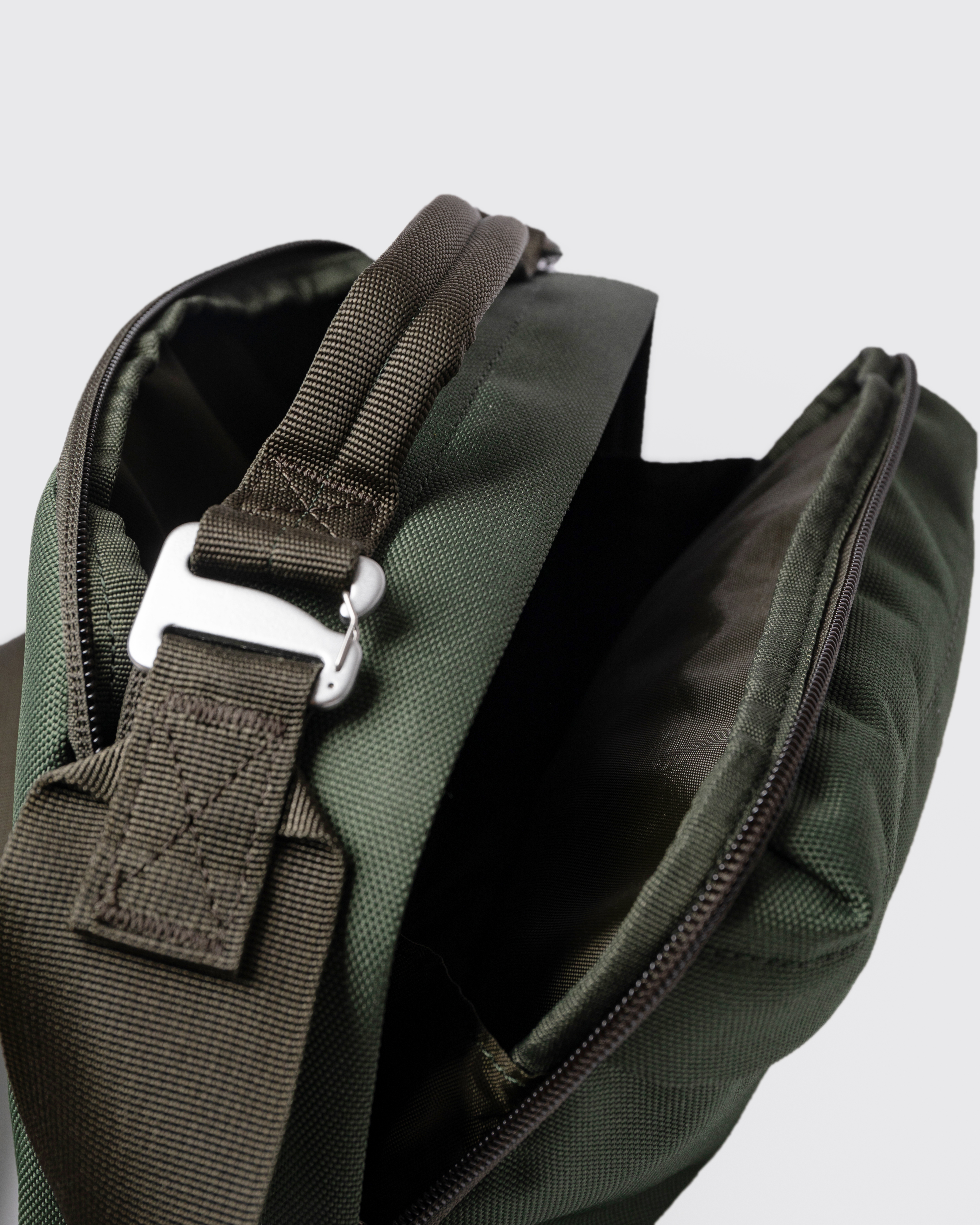 Sandqvist GO Shoulder Bag, vert. Gros plan sur la poignée avec boucle et deux compartiments à fermeture éclair.