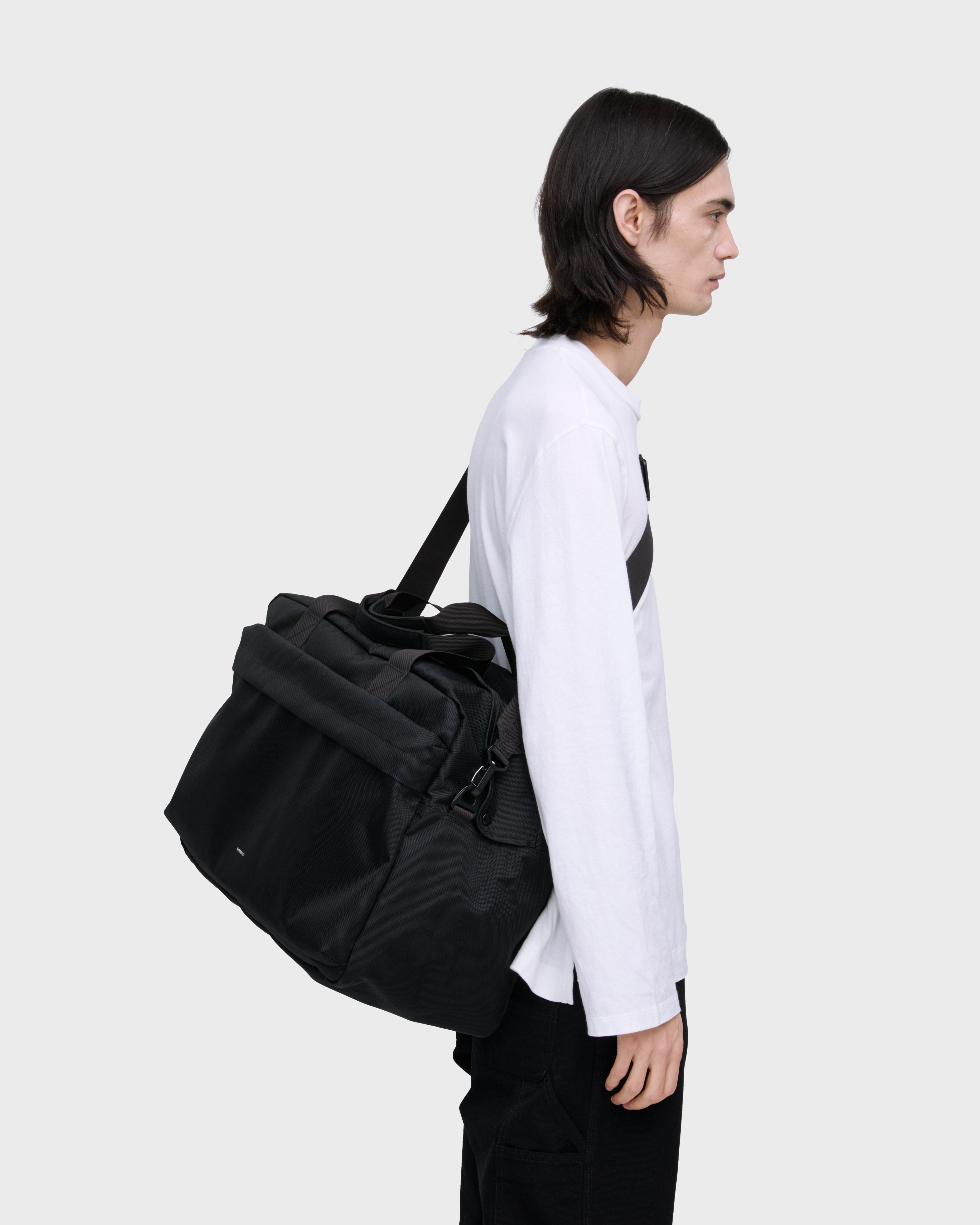 Male model wearing Sandqvist GO Weekender L, black. Side view, wearing the bag on one shoulder crossbody.